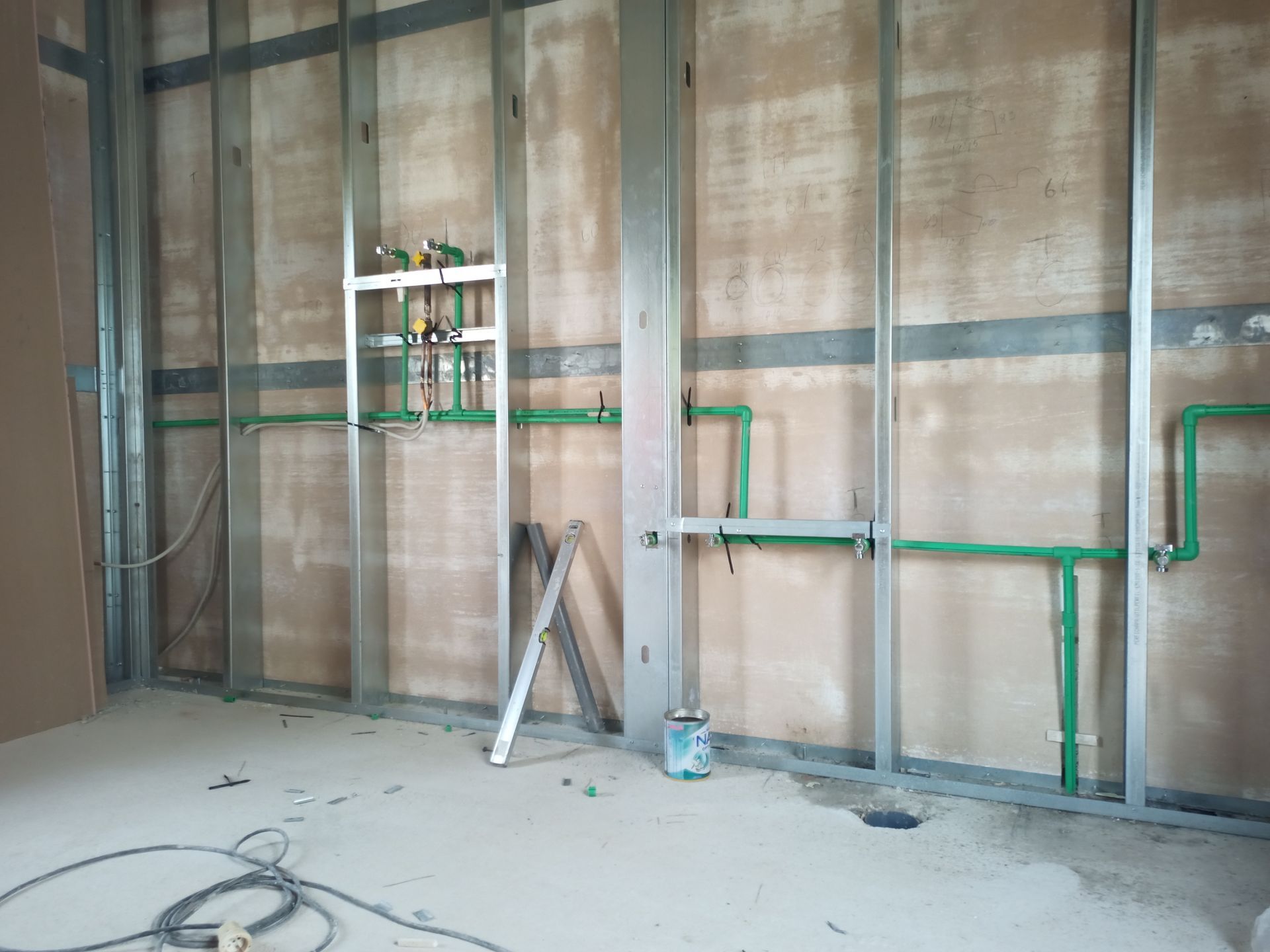 Parede interna em construção com estrutura metálica e tubulação hidráulica verde.