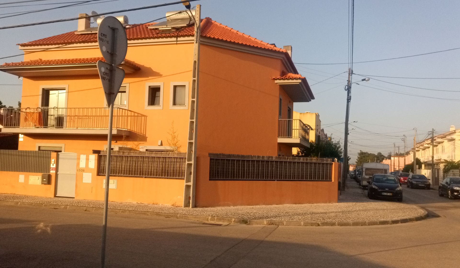 Casa laranja em um terreno de esquina, rua com carros, placa de trânsito em primeiro plano.