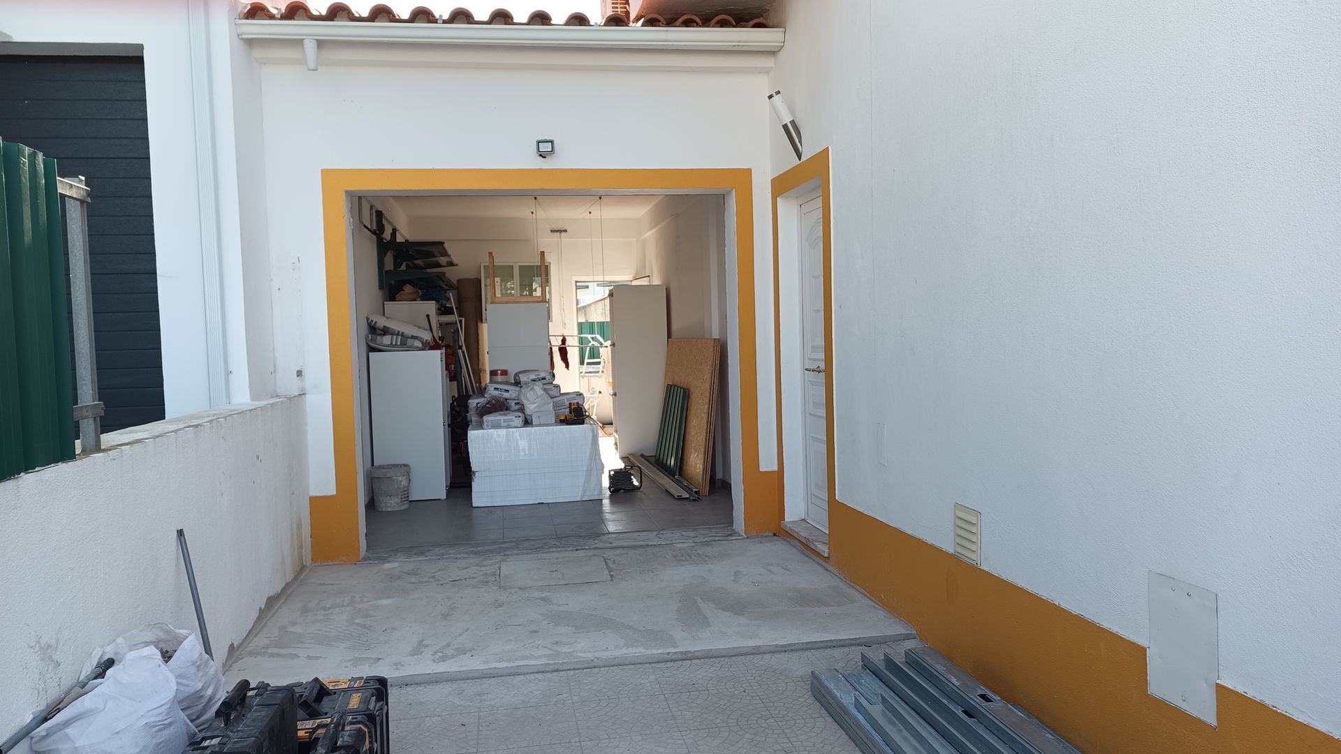 Vista externa para um interior luminoso e desorganizado através de uma porta aberta emoldurada em amarelo contra paredes brancas.