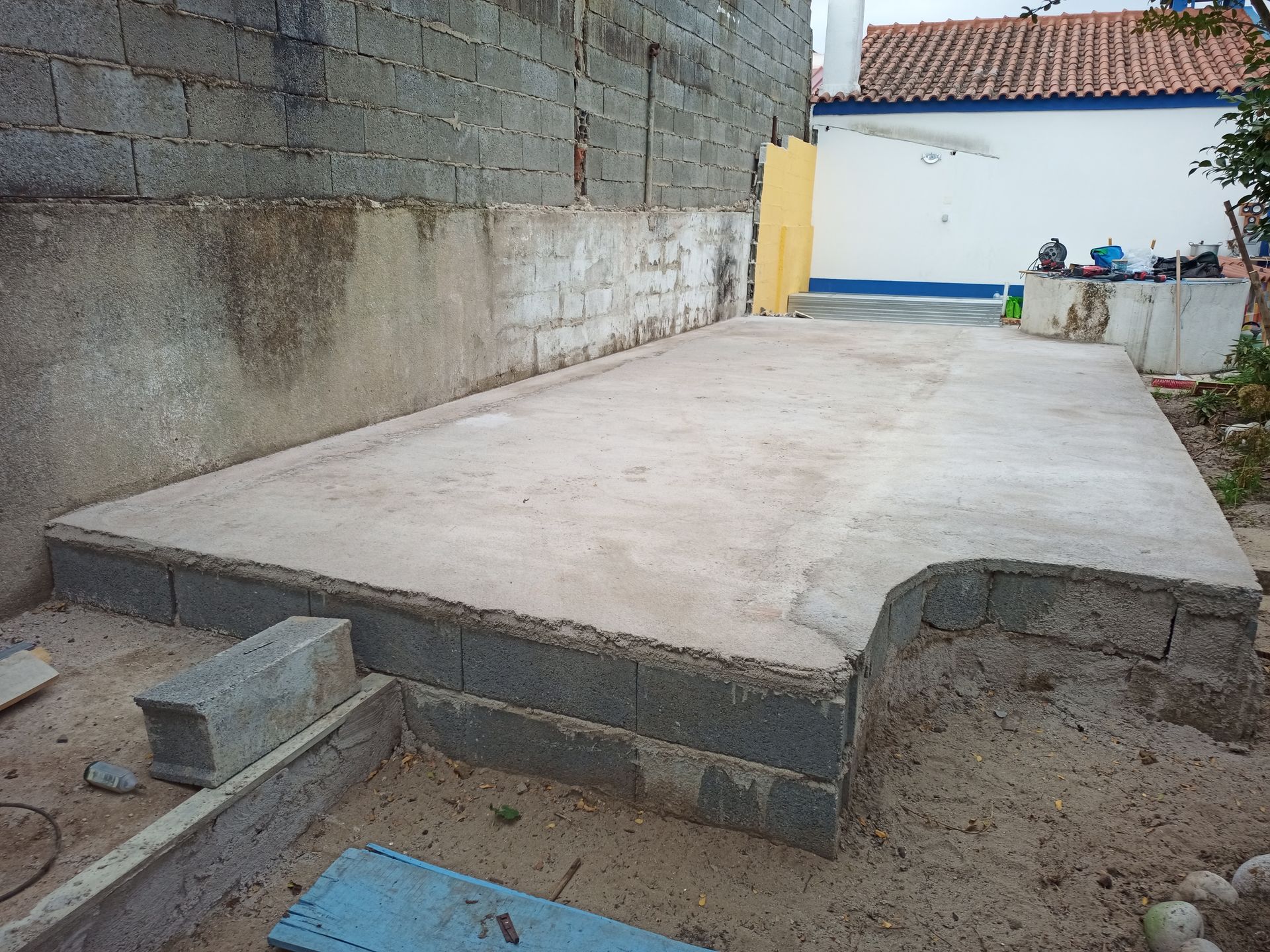 Canteiro de obras com laje de concreto, fundação em blocos de cimento e área arenosa ao redor.