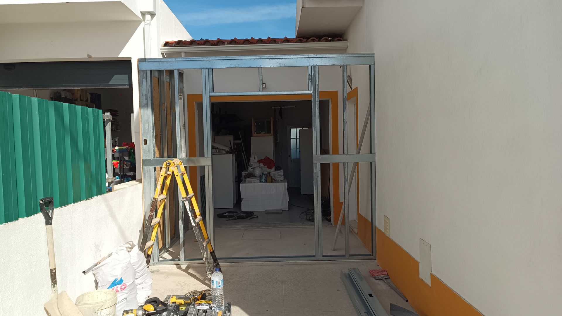 Estrutura metálica para uma porta em construção. Escada amarela e ferramentas estão à frente.