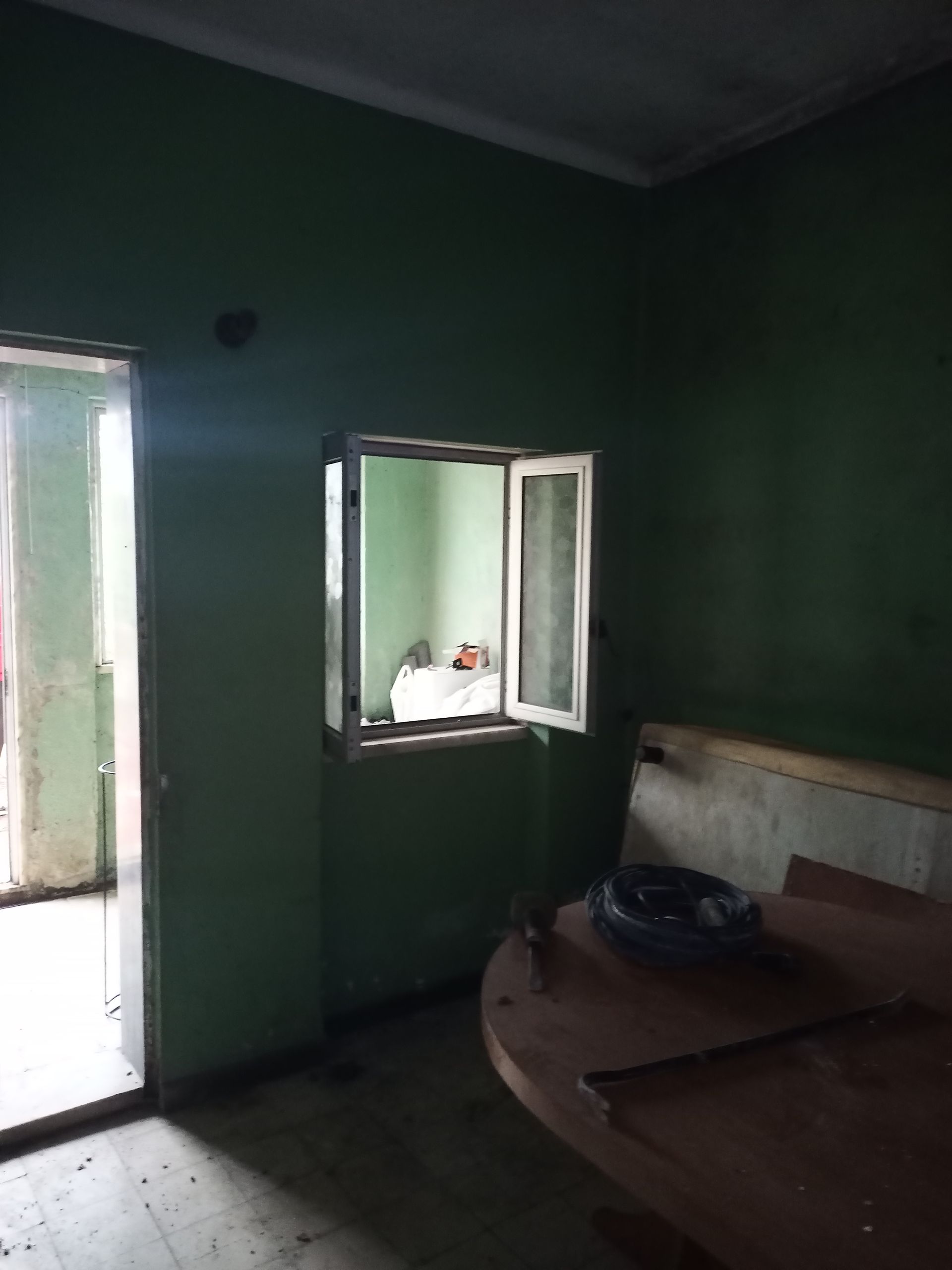 Sala verde com porta aberta, janela pequena e mesa de madeira.