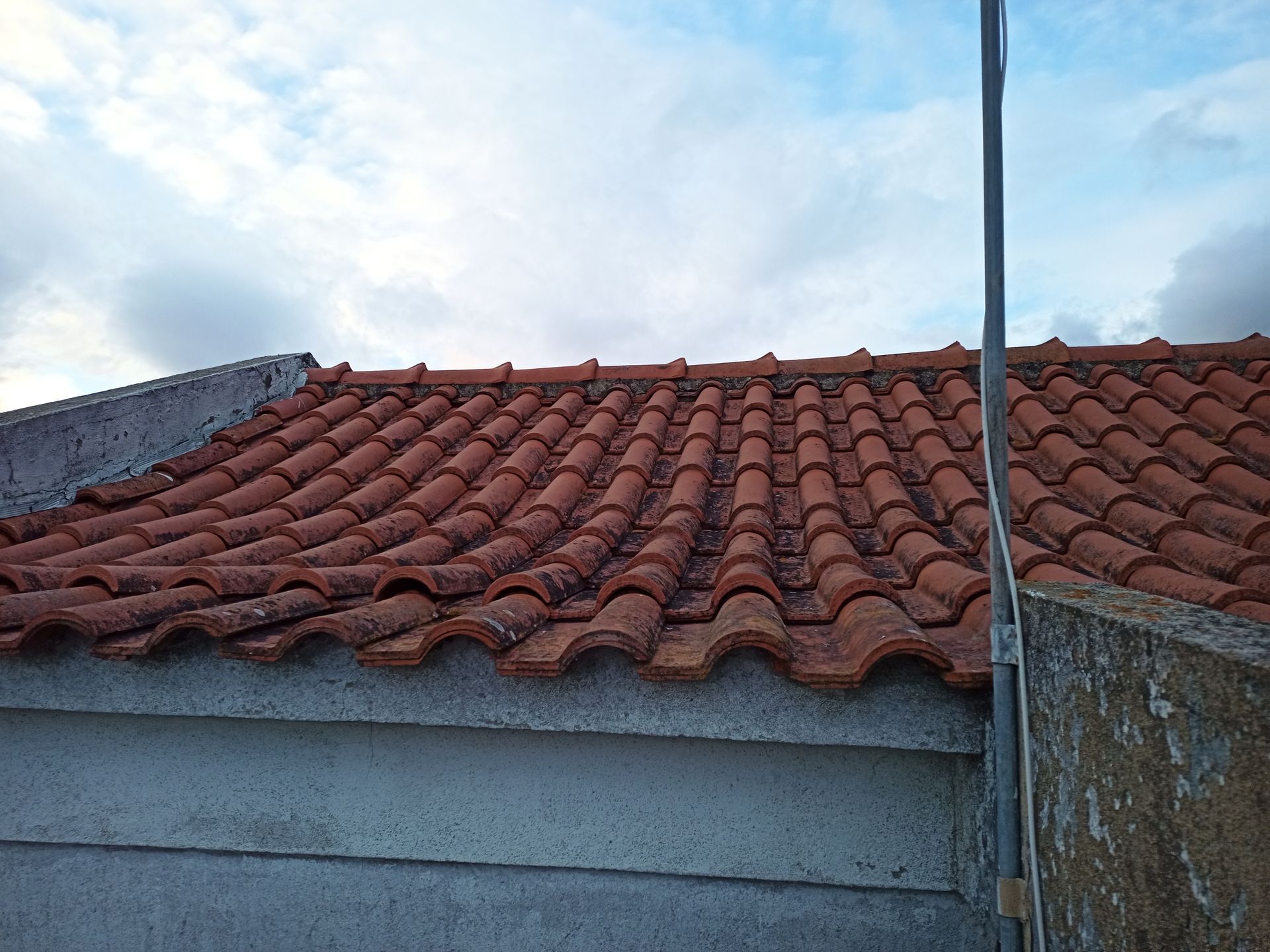 Telhado de telha vermelha em um prédio, sob um céu azul nublado.