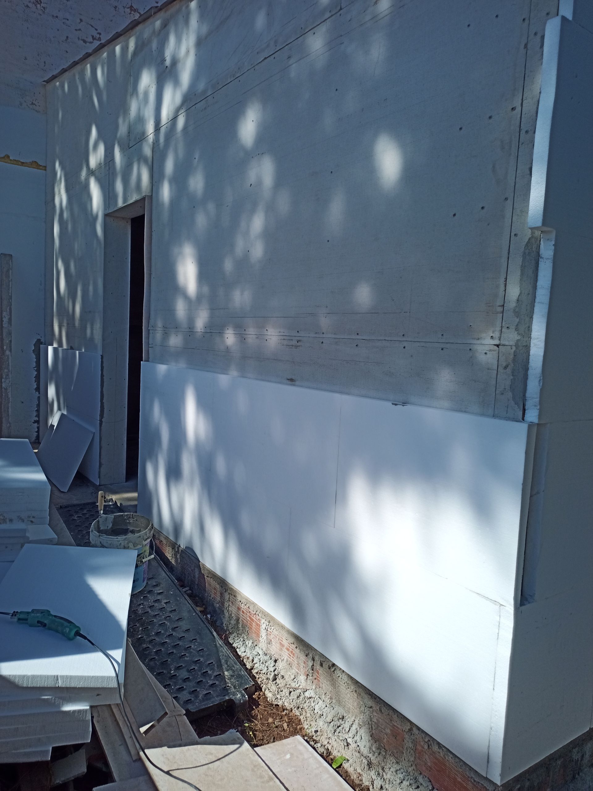 Parede externa com painéis isolantes brancos sendo instalados, ocultando parcialmente uma porta.