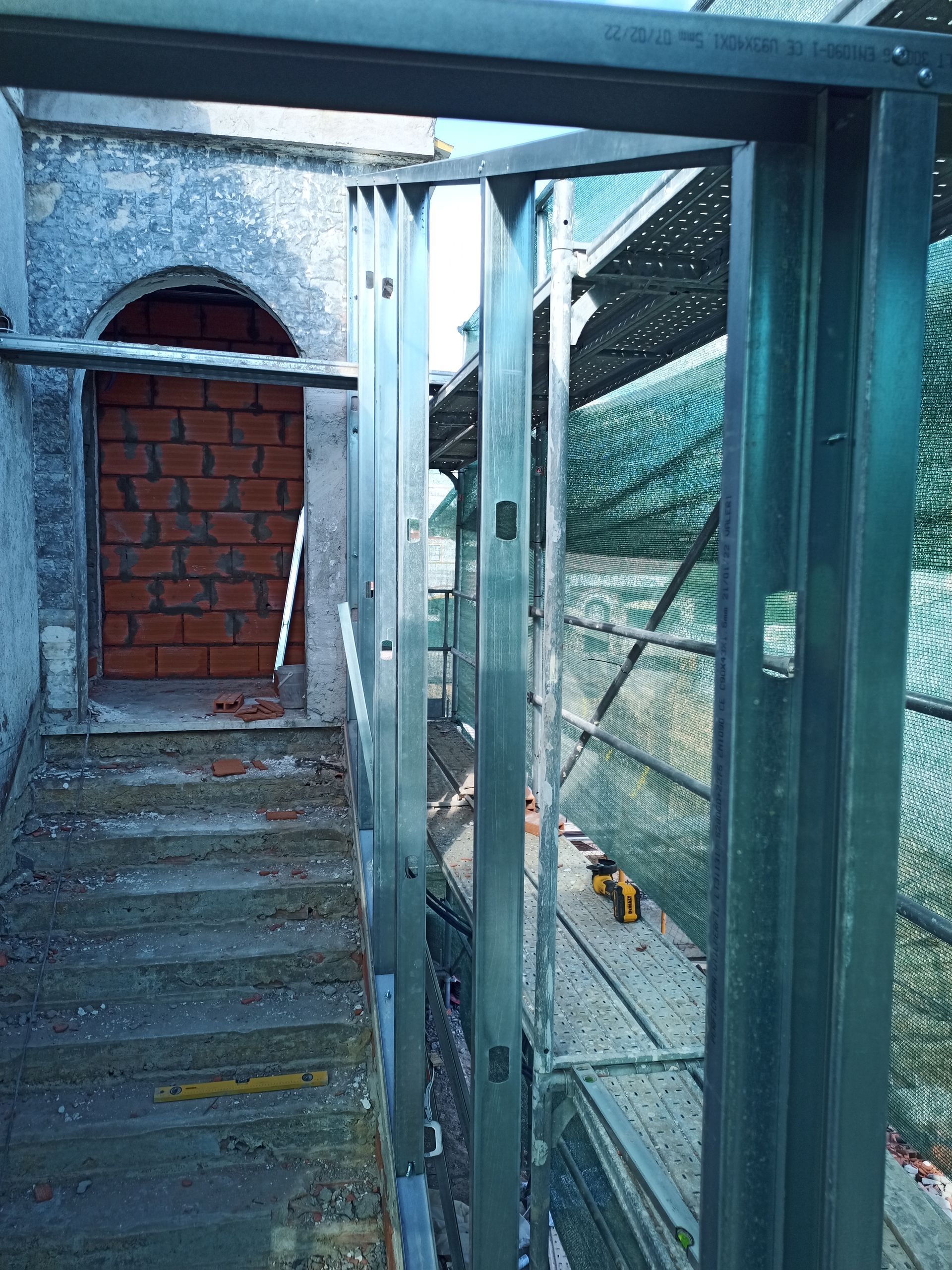 Estrutura metálica da porta na parte externa, entrada bloqueada com tijolos, andaimes visíveis.