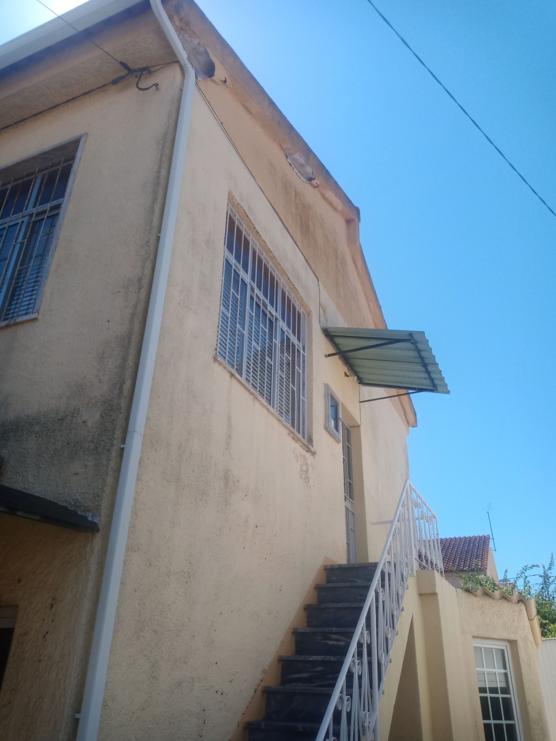 Prédio de dois andares com escadas, janelas e céu azul acima. Vista externa.