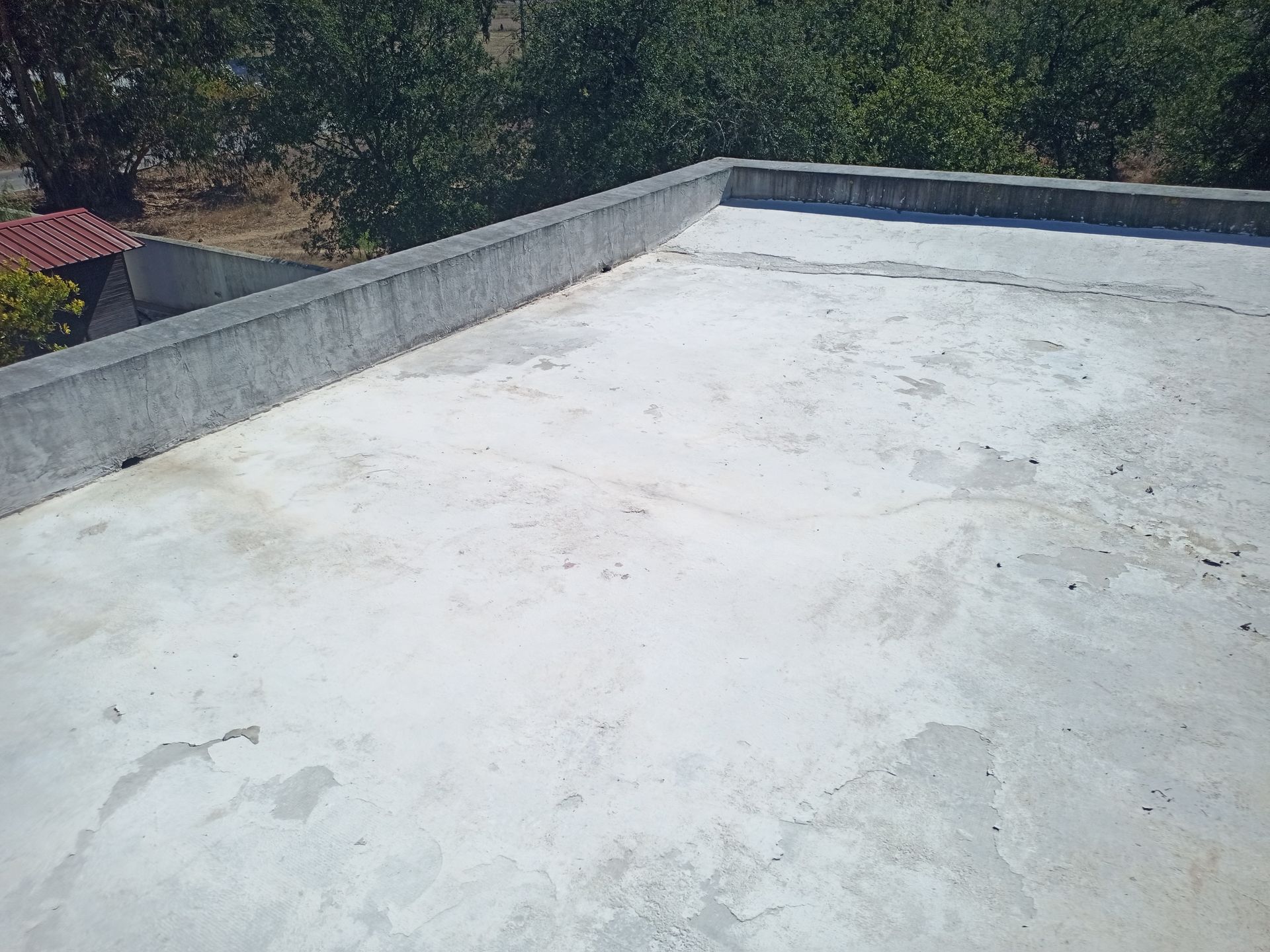 Um telhado plano de concreto com um muro de contenção baixo; árvores e um edifício são visíveis ao fundo.