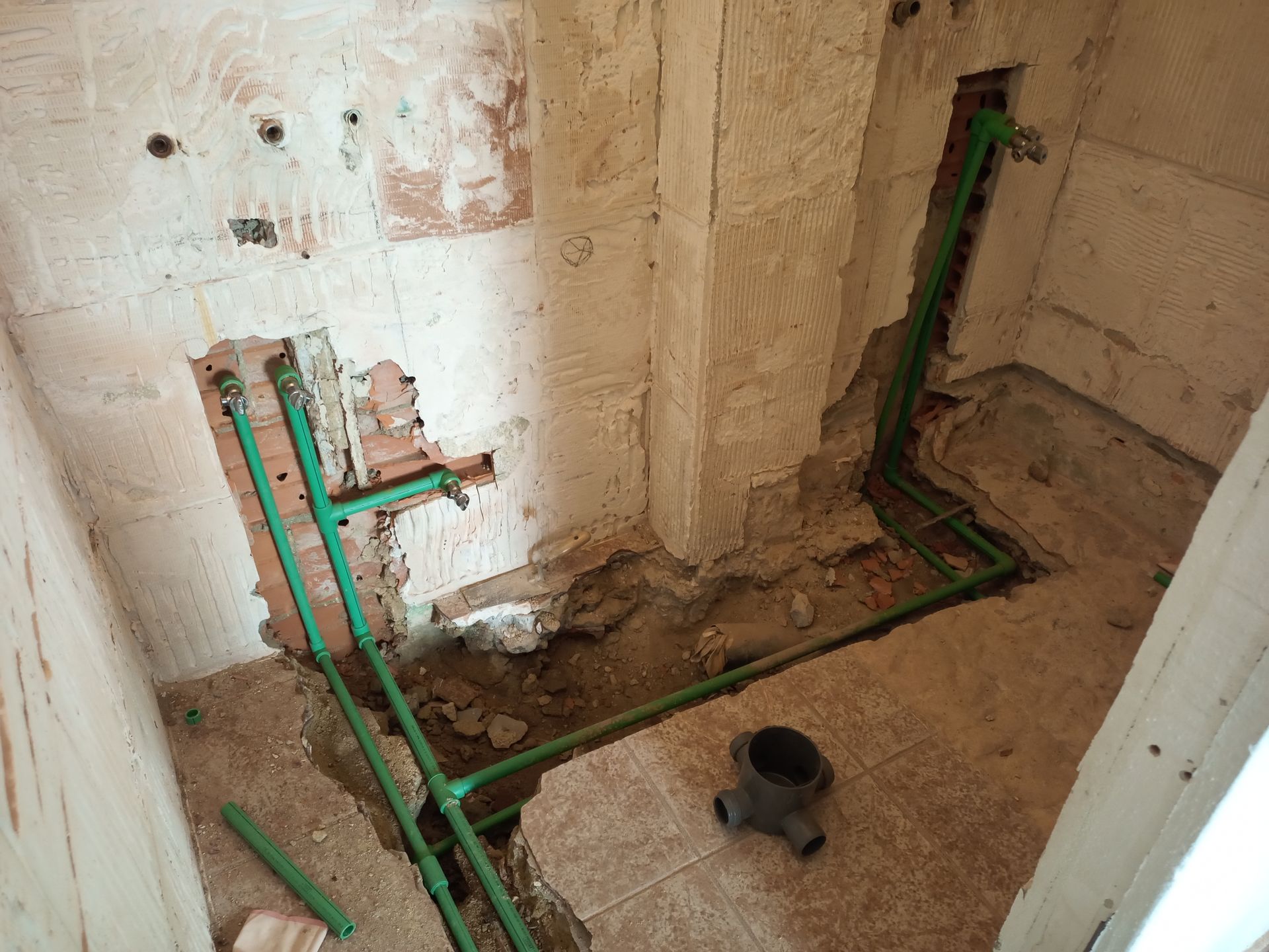 Instalação hidráulica preliminar com tubos verdes em um banheiro parcialmente demolido.