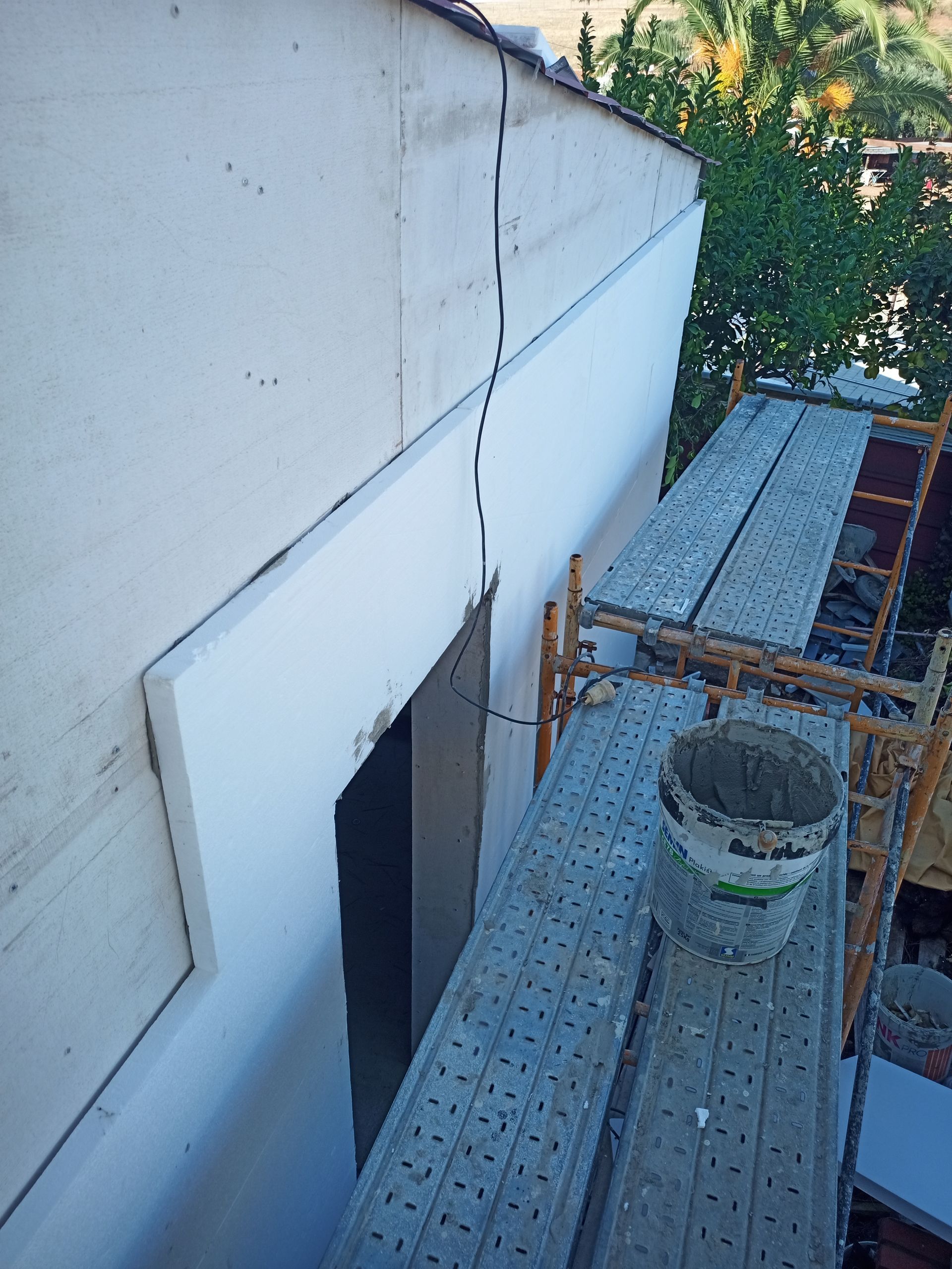 Exterior de um edifício com andaimes, uma porta aberta e um balde de material.