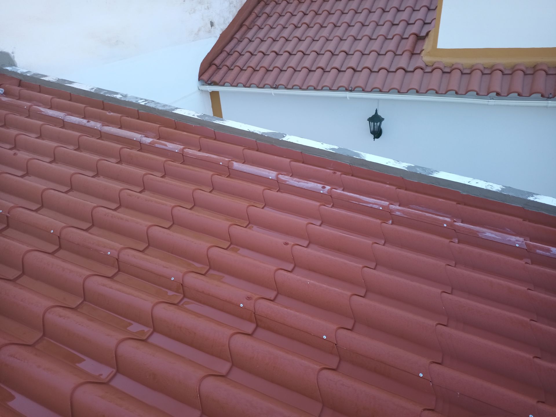 Telhado de telha vermelha de um edifício com parede branca e luminária decorativa.