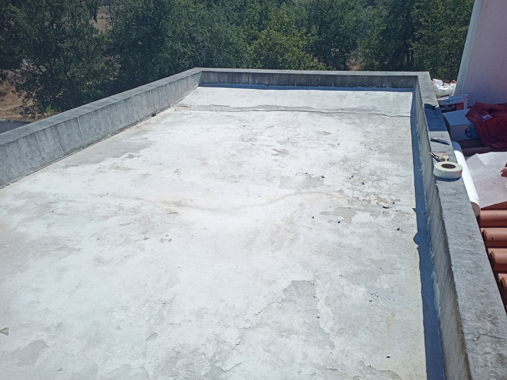 Cobertura de concreto com uma pequena barreira de concreto. Árvores verdes ao fundo, visíveis sob um céu claro.