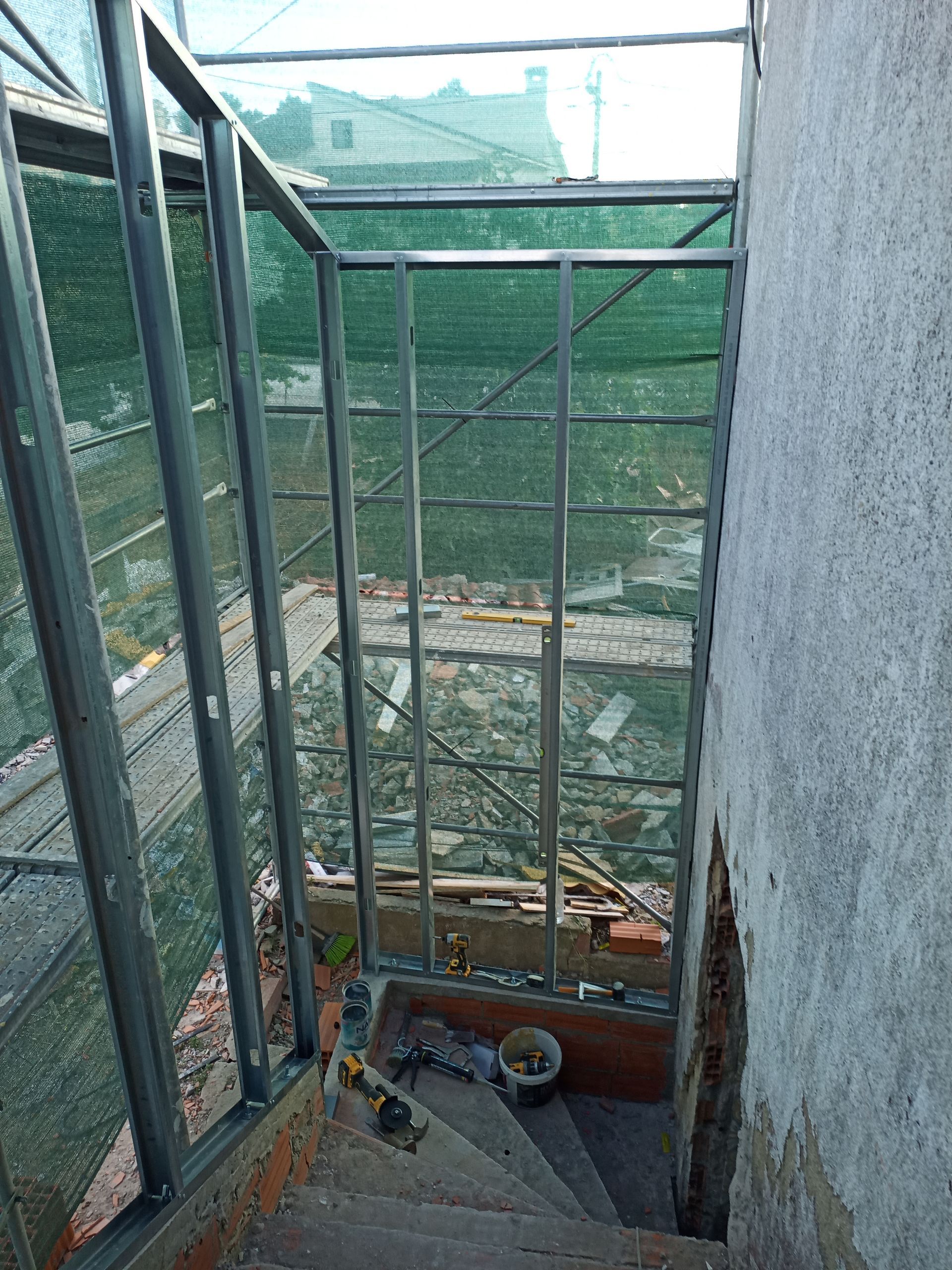 Estrutura metálica sobre uma escada descendente, tela verde e uma abertura para o exterior.