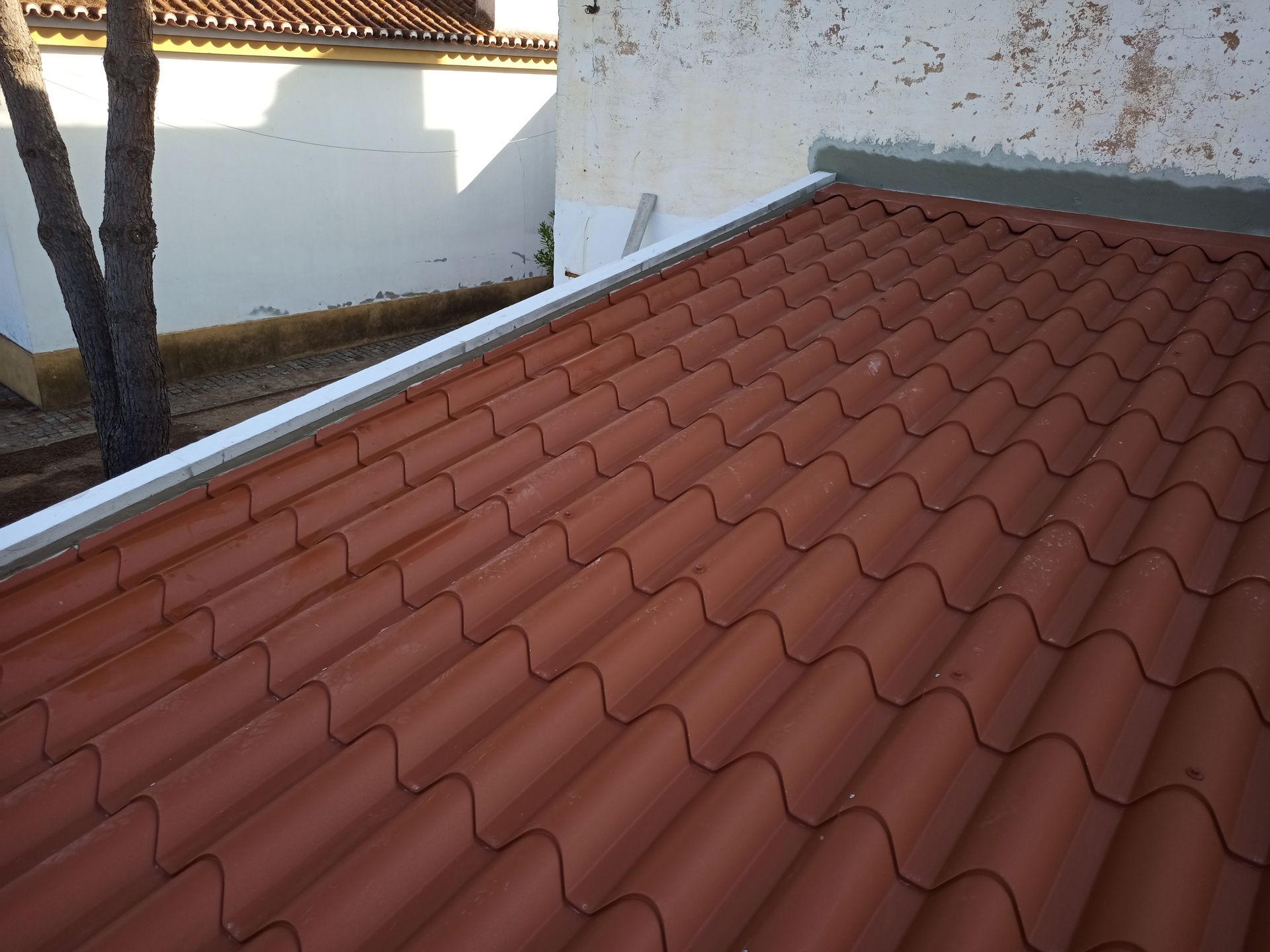 Telhado de telha vermelha com detalhes em branco e uma parede branca ao fundo.
