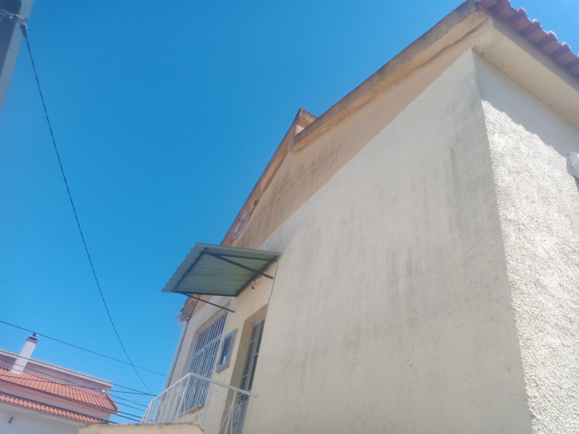 Prédio bege com um pequeno toldo sobre uma janela, contra um céu azul brilhante.