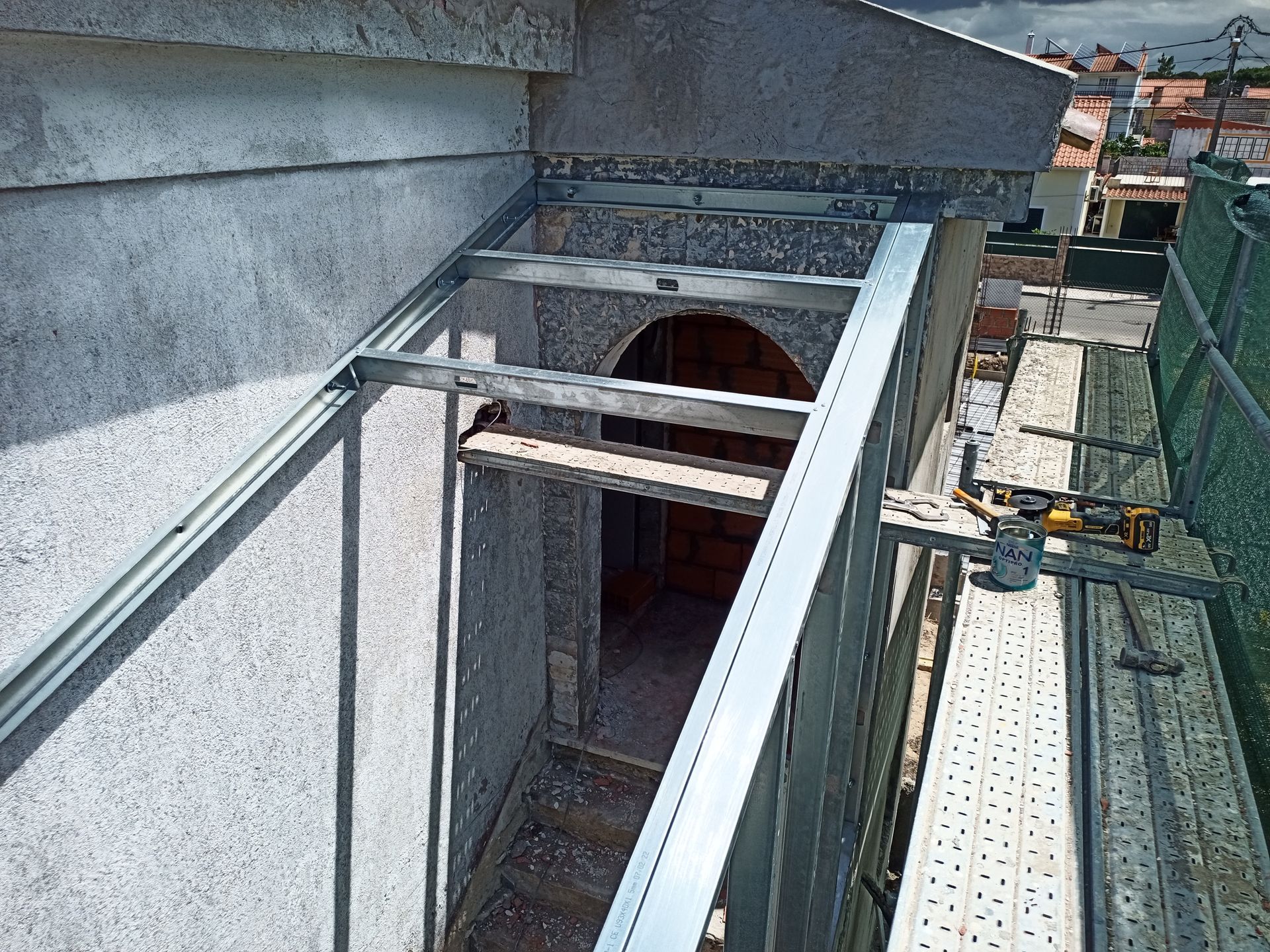Estrutura metálica para uma fachada de edifício, com andaimes e vislumbre de uma porta.