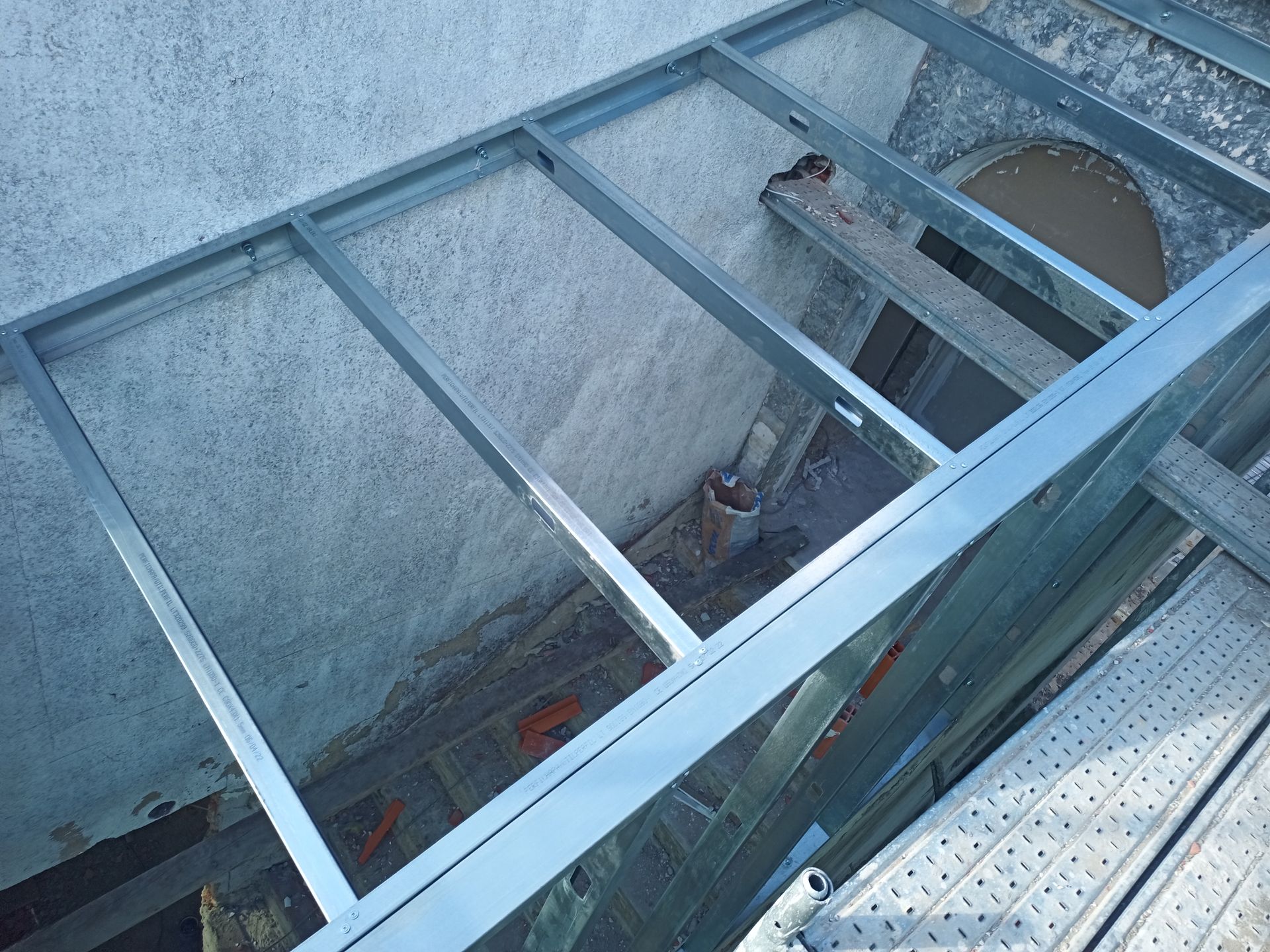 Estrutura metálica contra uma parede texturizada, com uma abertura e um cano visíveis.