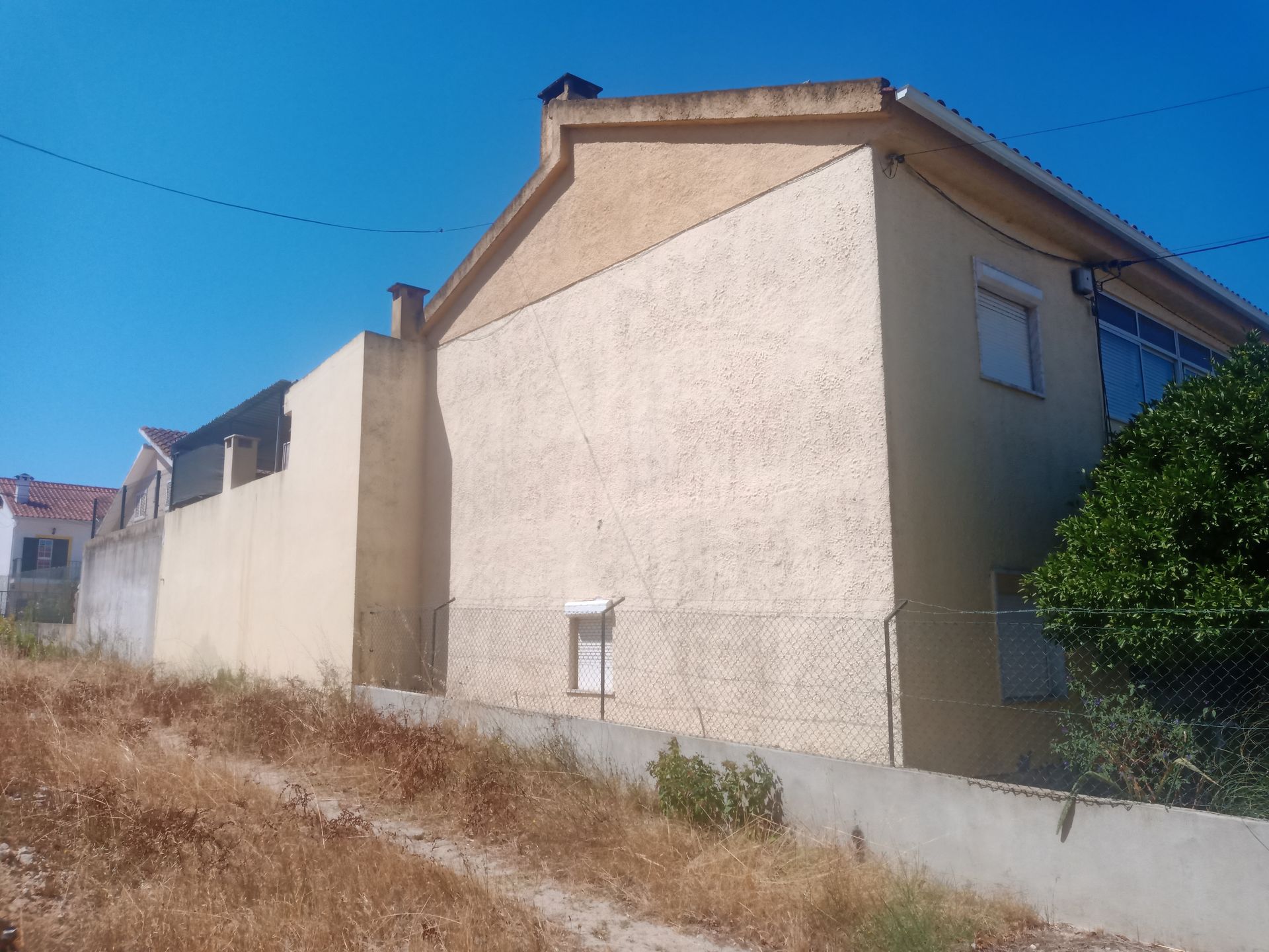 Prédio de estuque bege em uma encosta contra um céu azul, com uma chaminé e uma pequena janela visíveis.