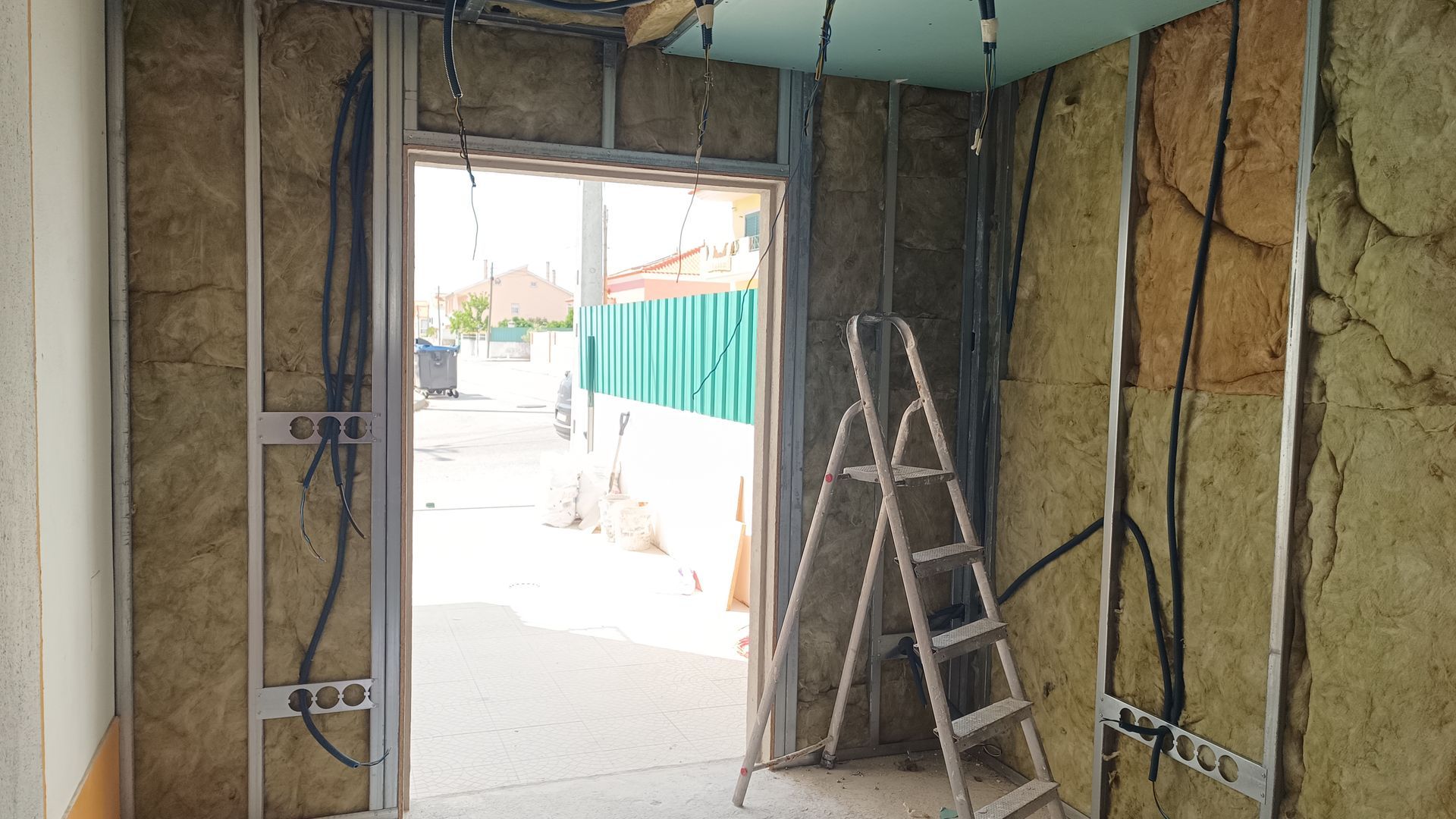 Estrutura interna: estrutura metálica com isolamento, porta aberta, escada interna. Fiação aparente, paredes inacabadas, vista para o exterior.