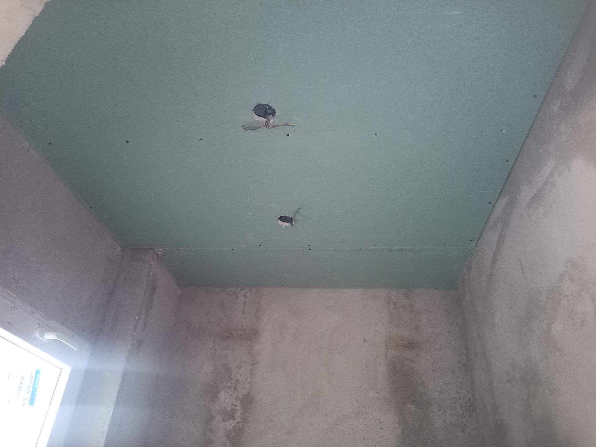 Teto com drywall verde instalado, duas luminárias visíveis, cômodo com paredes de concreto.