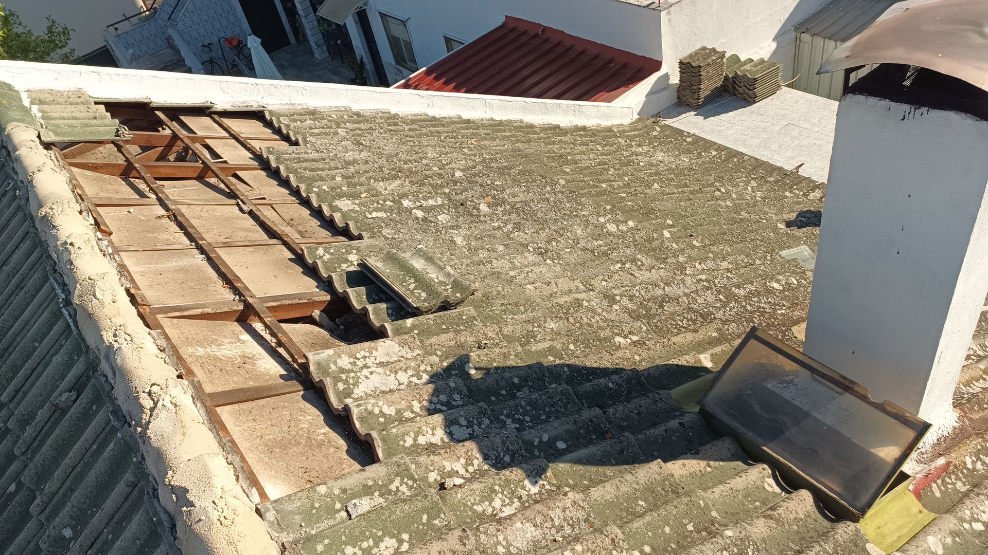 Telhado danificado com telhas quebradas, vigas expostas e uma chaminé.