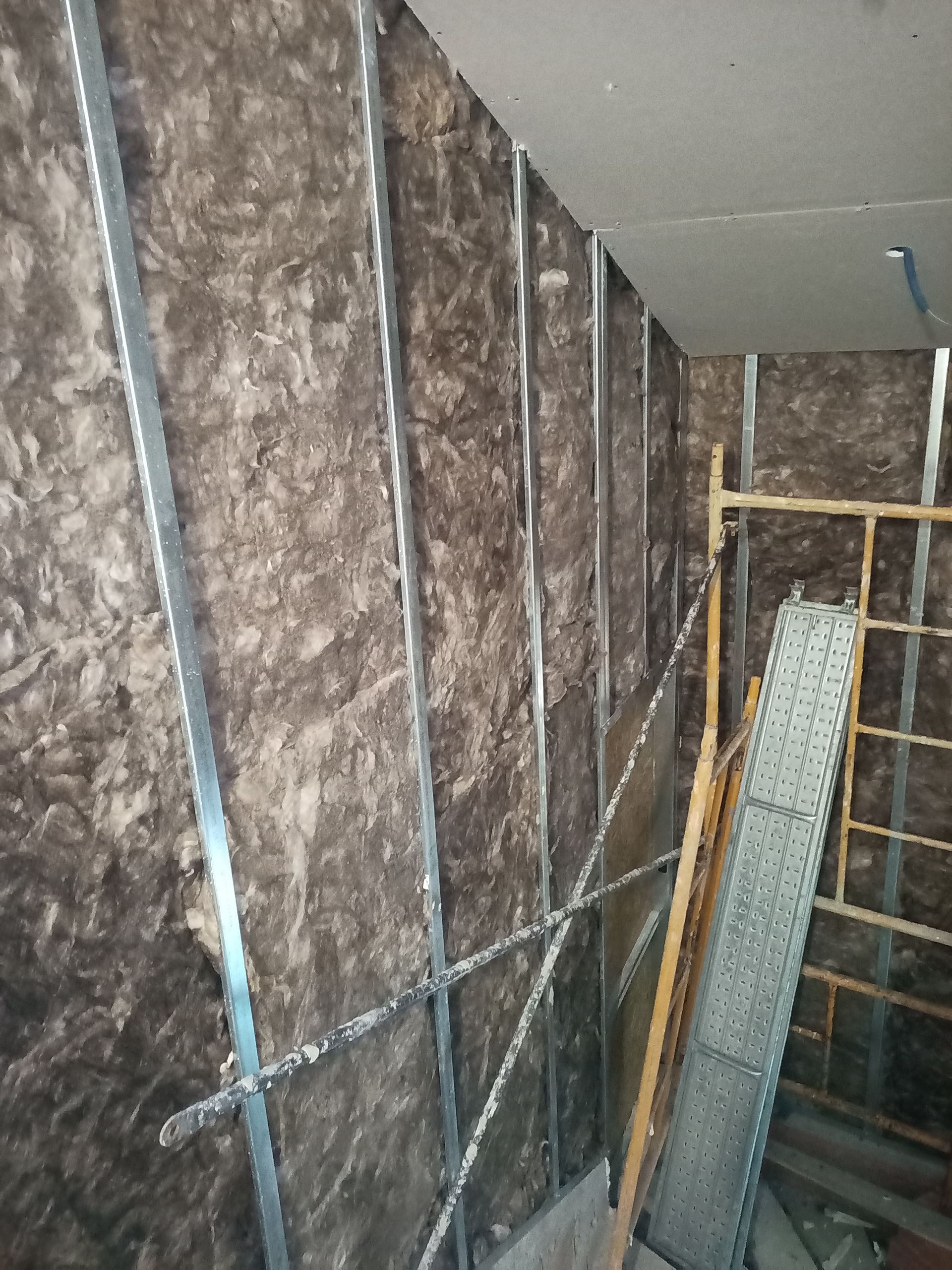 Parede interna em construção; isolamento entre perfis metálicos, teto inacabado visível.