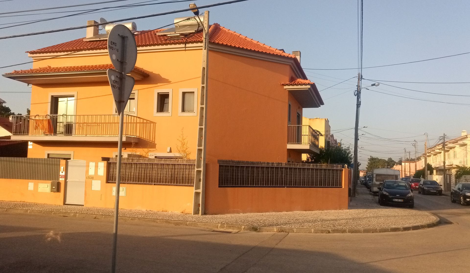 Prédio laranja de dois andares em um terreno de esquina, com carros na rua ao fundo.