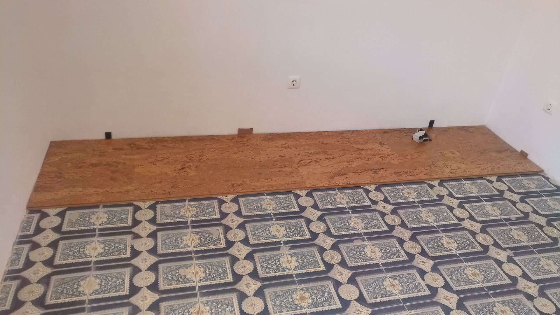 Painel de cortiça parcialmente instalado sobre piso de azulejo e contra uma parede branca.