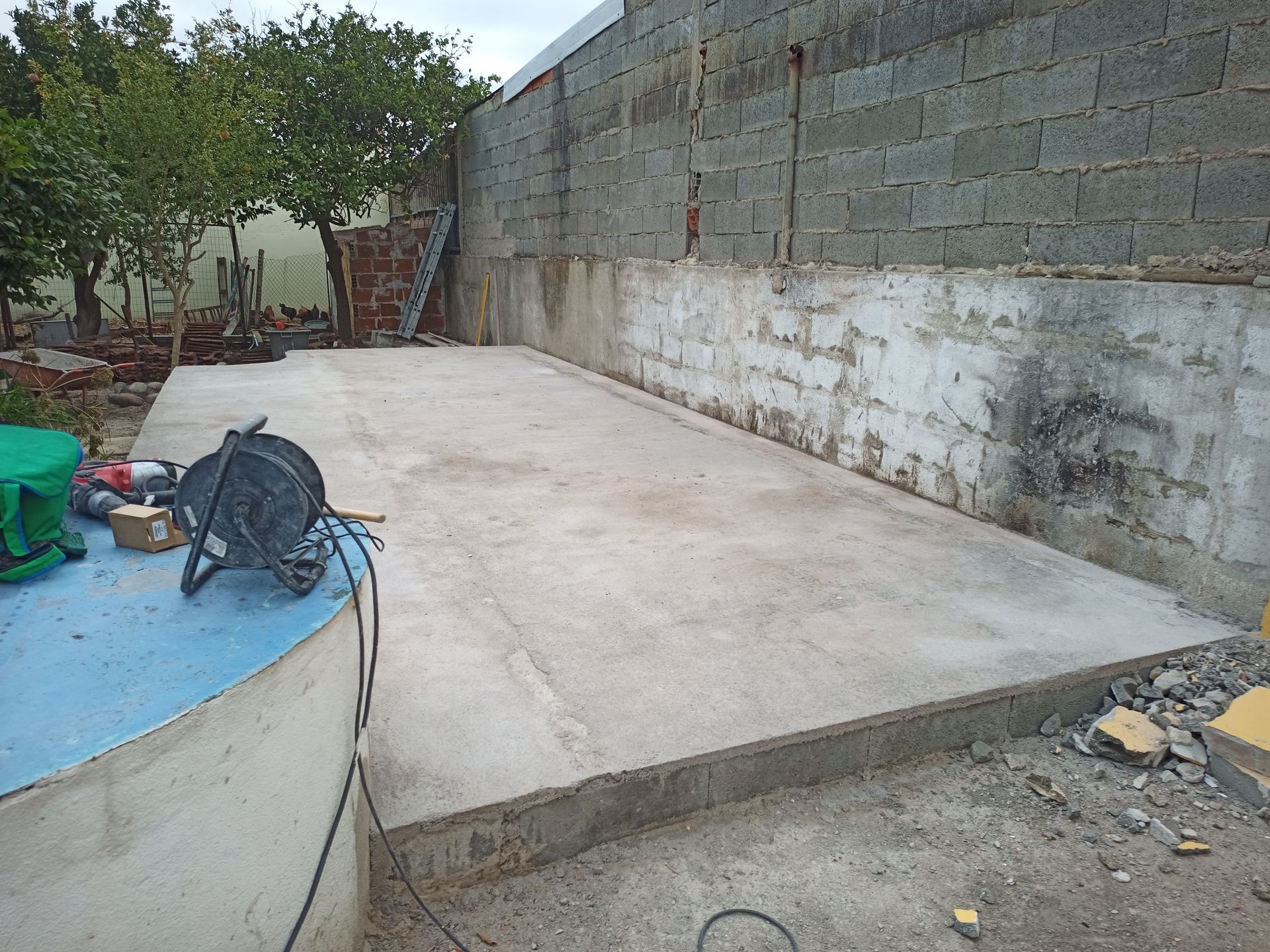 Placa de concreto em um quintal, ao lado de um muro de blocos e uma estrutura curva azul.