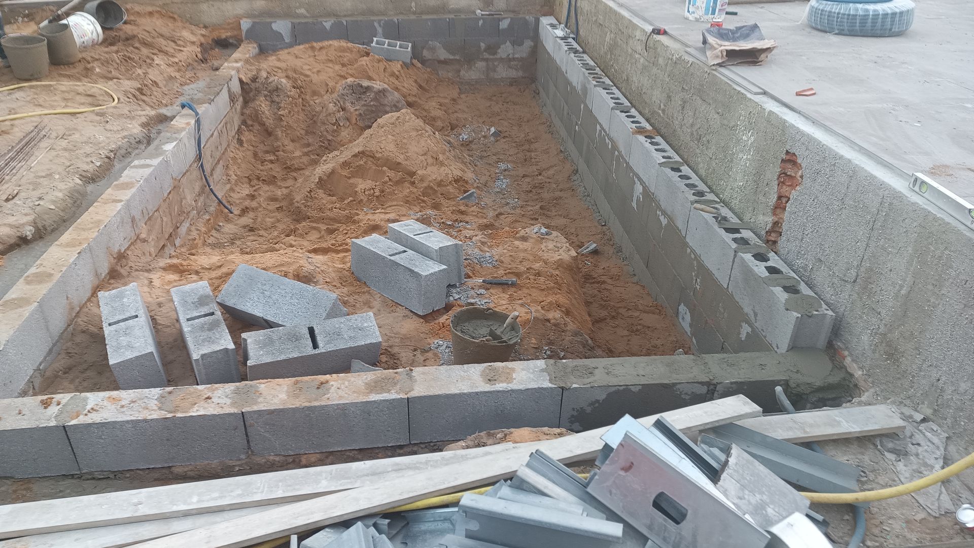 Canteiro de obras: Construção de uma fundação de blocos de concreto, com areia e blocos no interior.