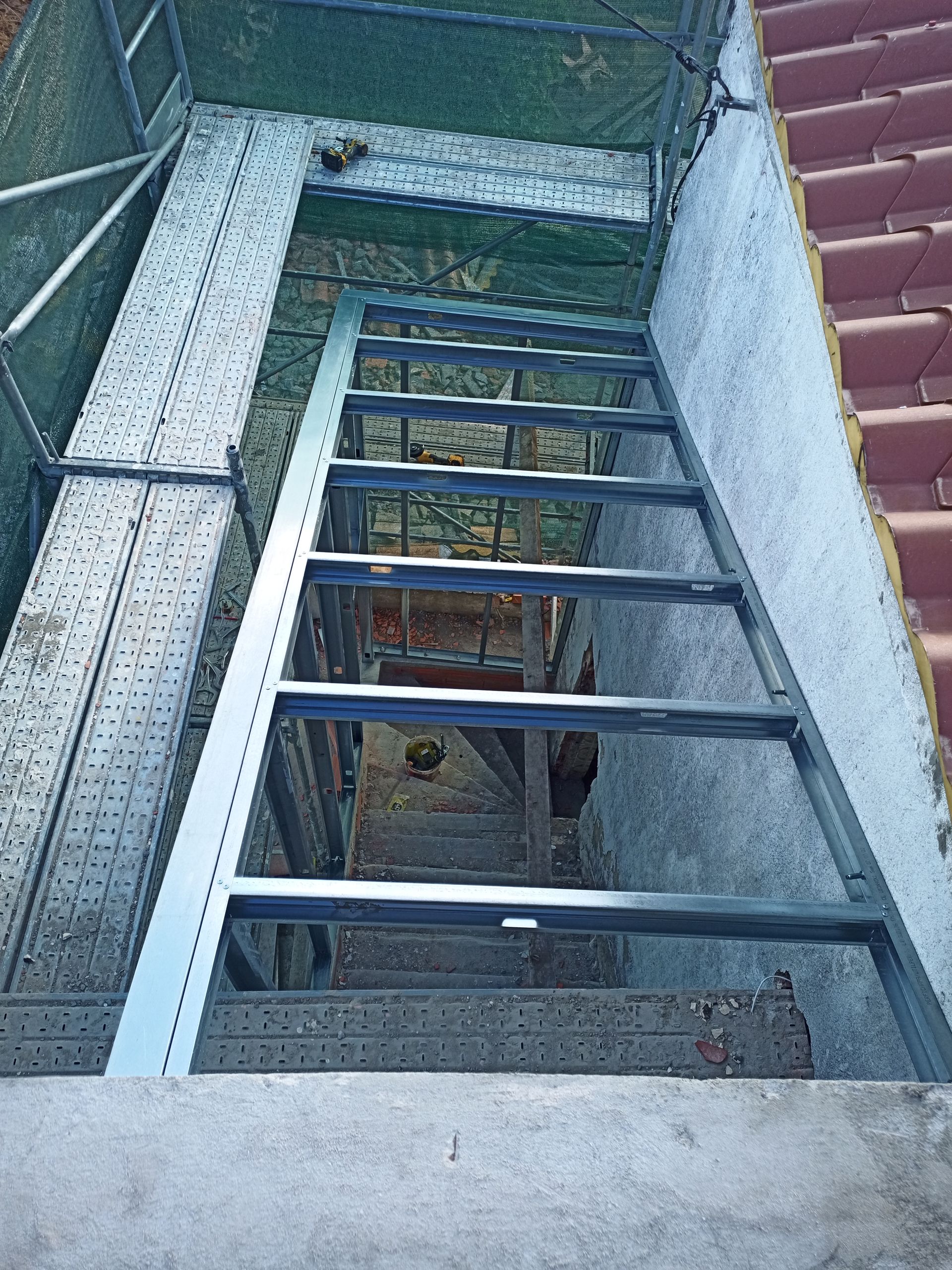 Escada metálica que desce por uma abertura escura em um prédio; vista de cima.