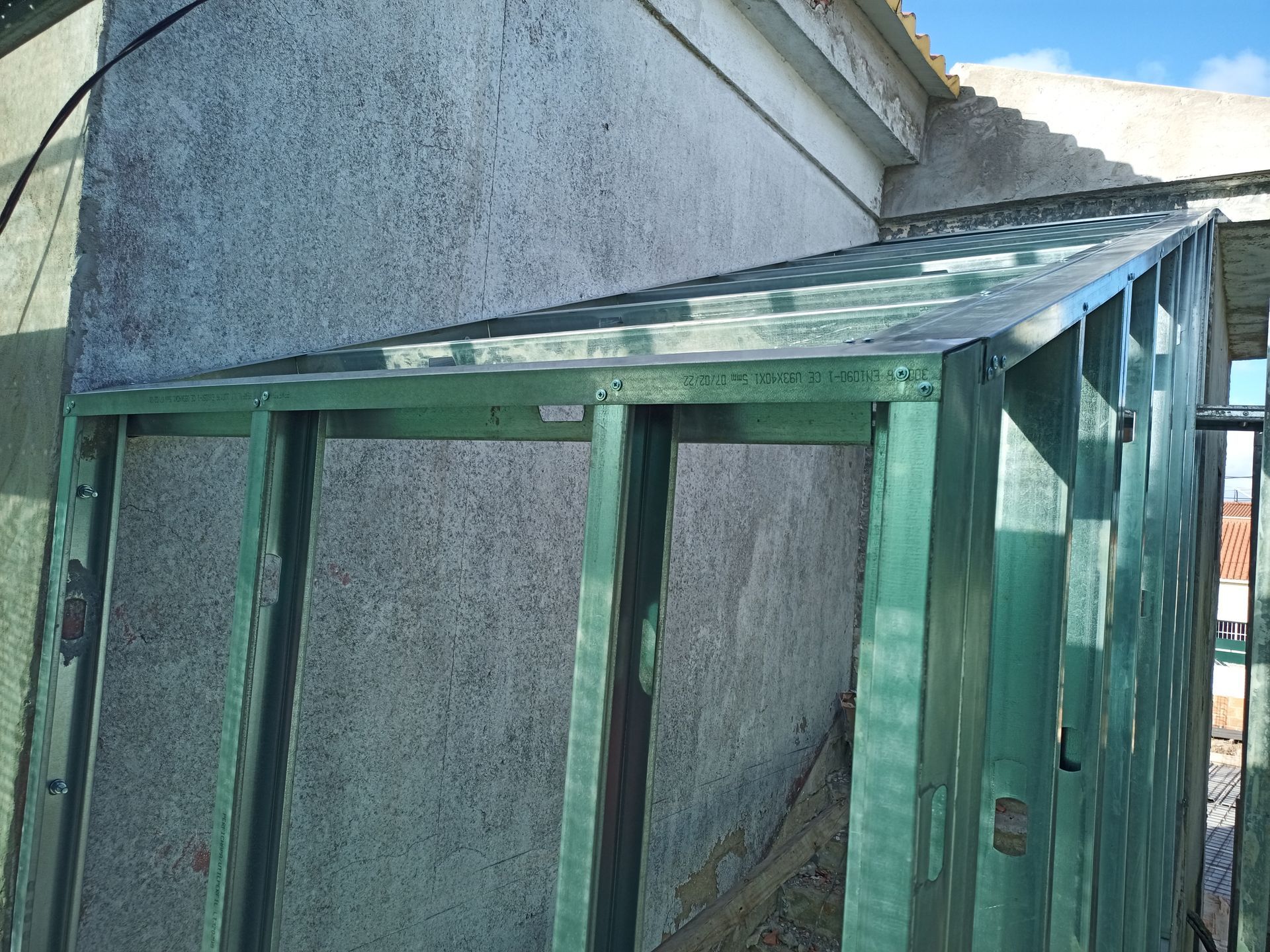 Estrutura metálica verde com telhado inclinado, fixada a uma parede de estuque de cor clara.