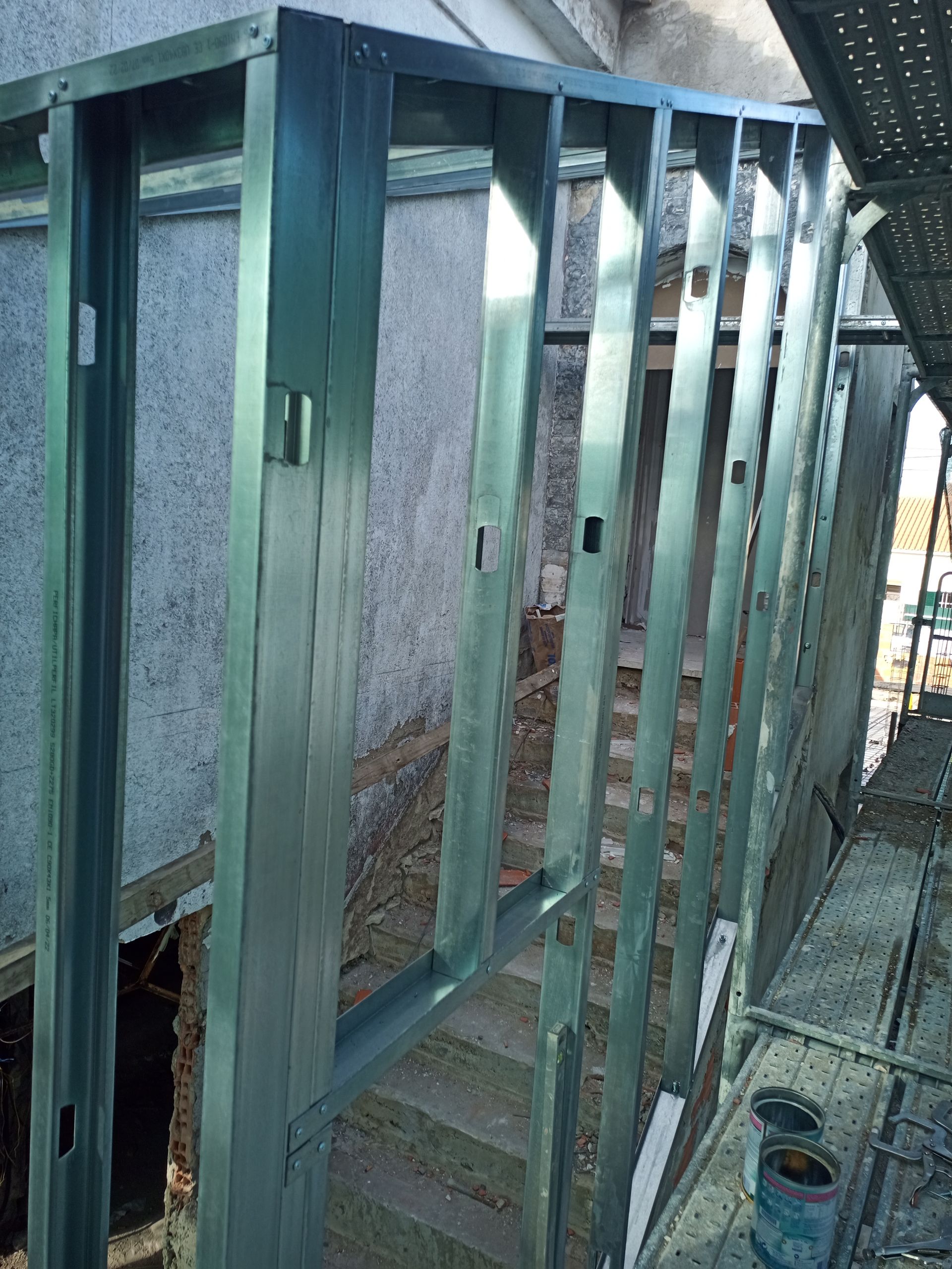 Estrutura metálica para parede e porta, mostrando os montantes e uma estrutura parcialmente construída na parte externa.