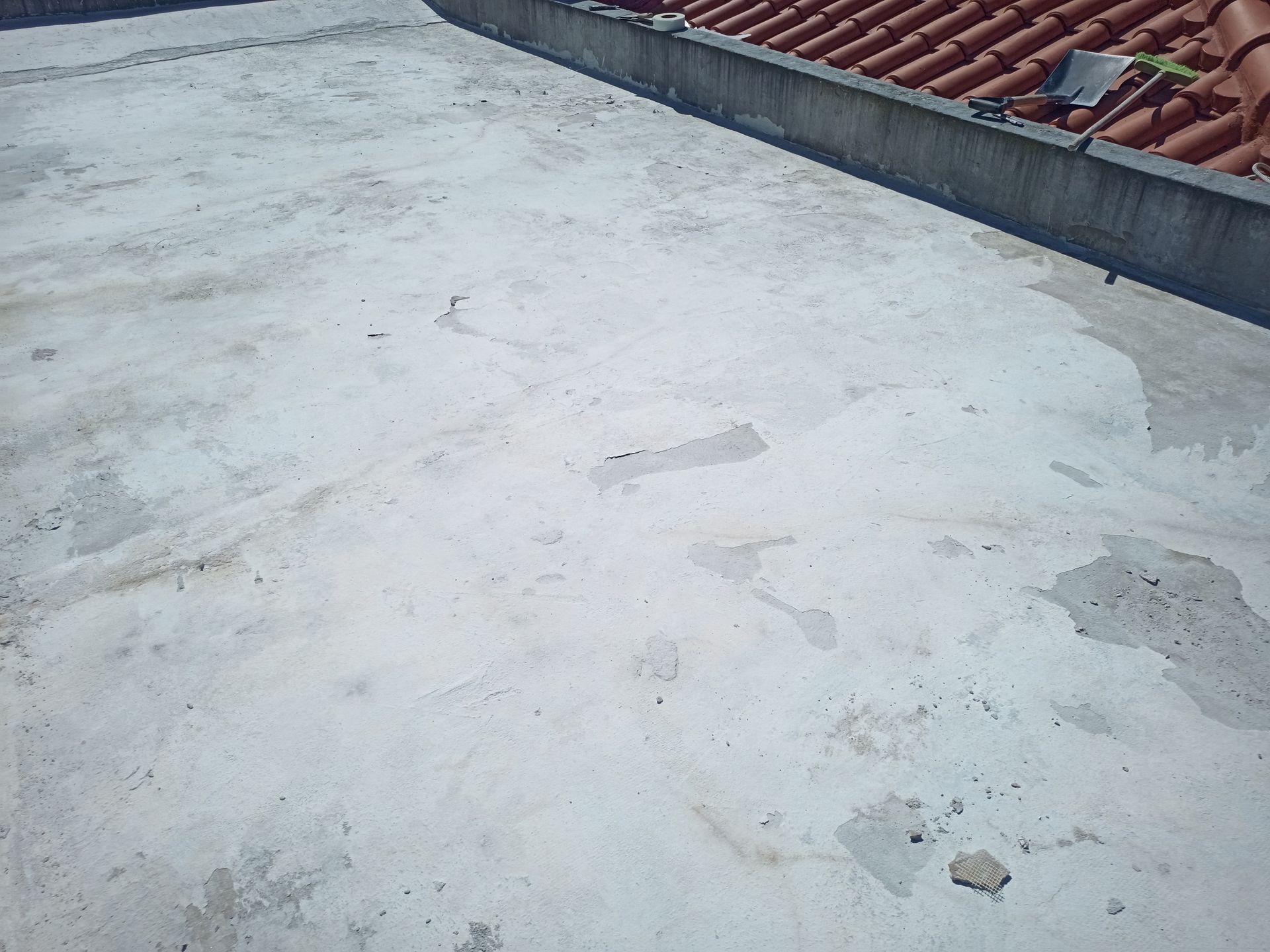 Telhado de concreto cinza com seções em tons mais claros, próximo a um telhado de telhas vermelhas.