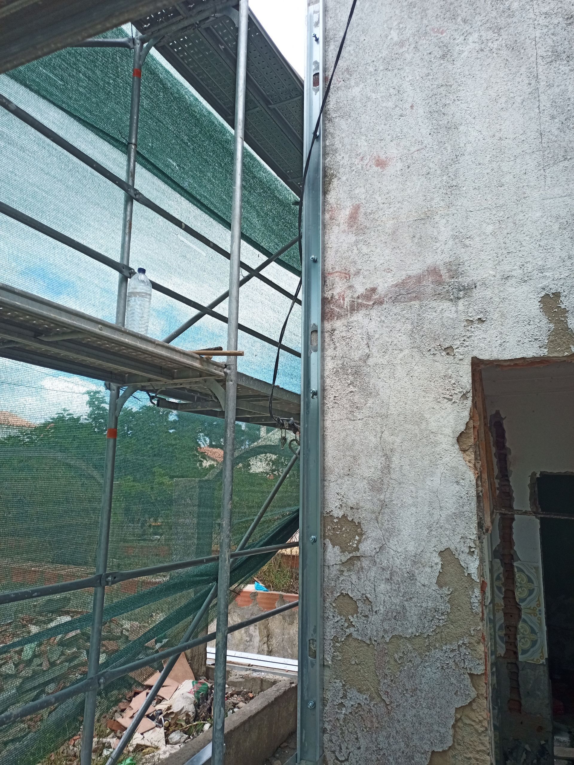 Andaimes junto à parede deteriorada de um edifício. Uma rede de segurança verde está fixada aos andaimes.
