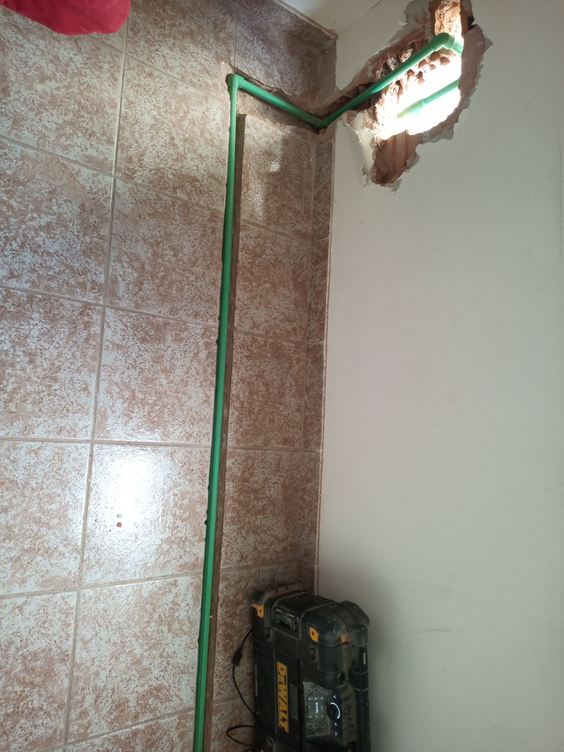 Tubos verdes instalados na parede, conectados a uma abertura danificada. Uma caixa de ferramentas está no chão.