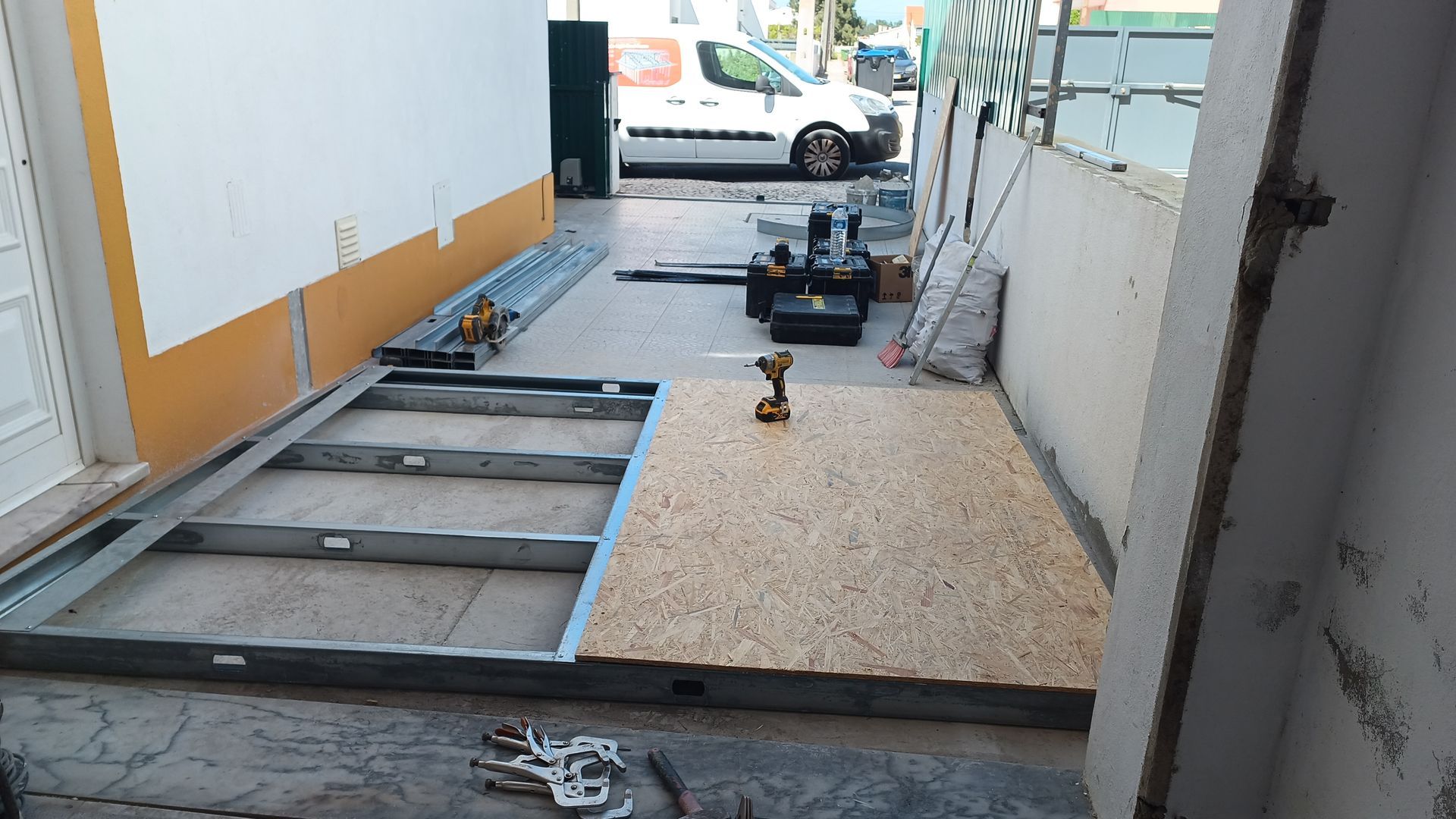 Canteiro de obras: estrutura de aço e piso de madeira compensada já instalados; ferramentas visíveis.