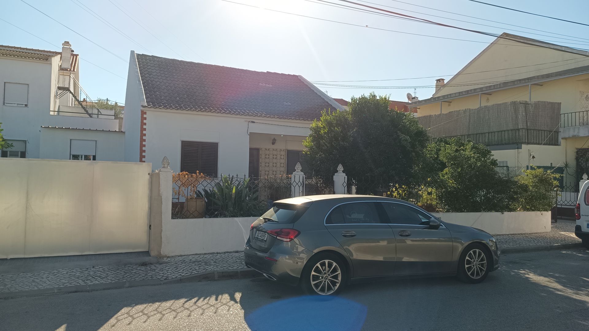 Um carro cinza estacionado em uma rua em frente a uma casa branca com telhado marrom e um pequeno jardim.