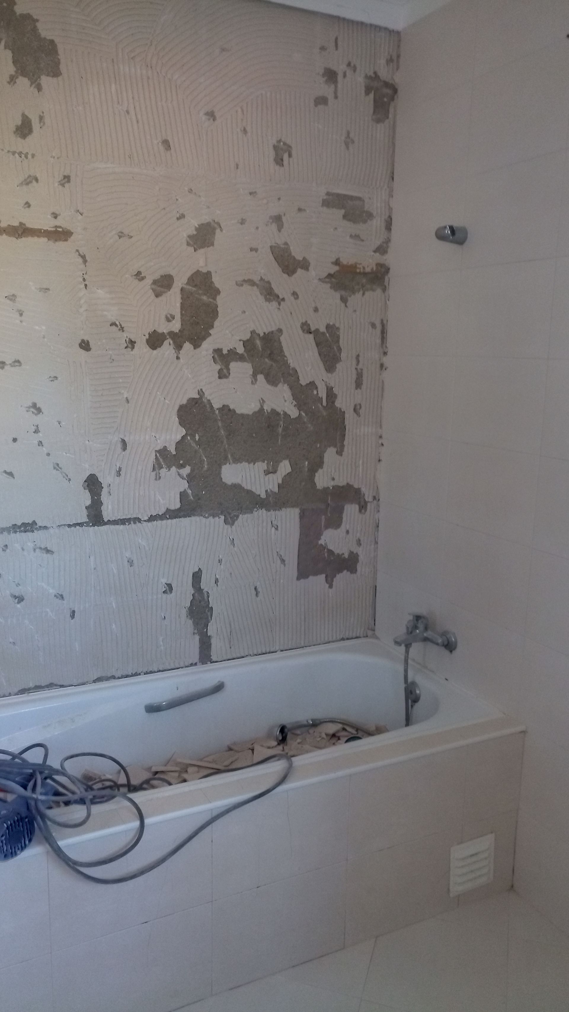 Parede do banheiro com reboco danificado acima da banheira, obra em andamento.
