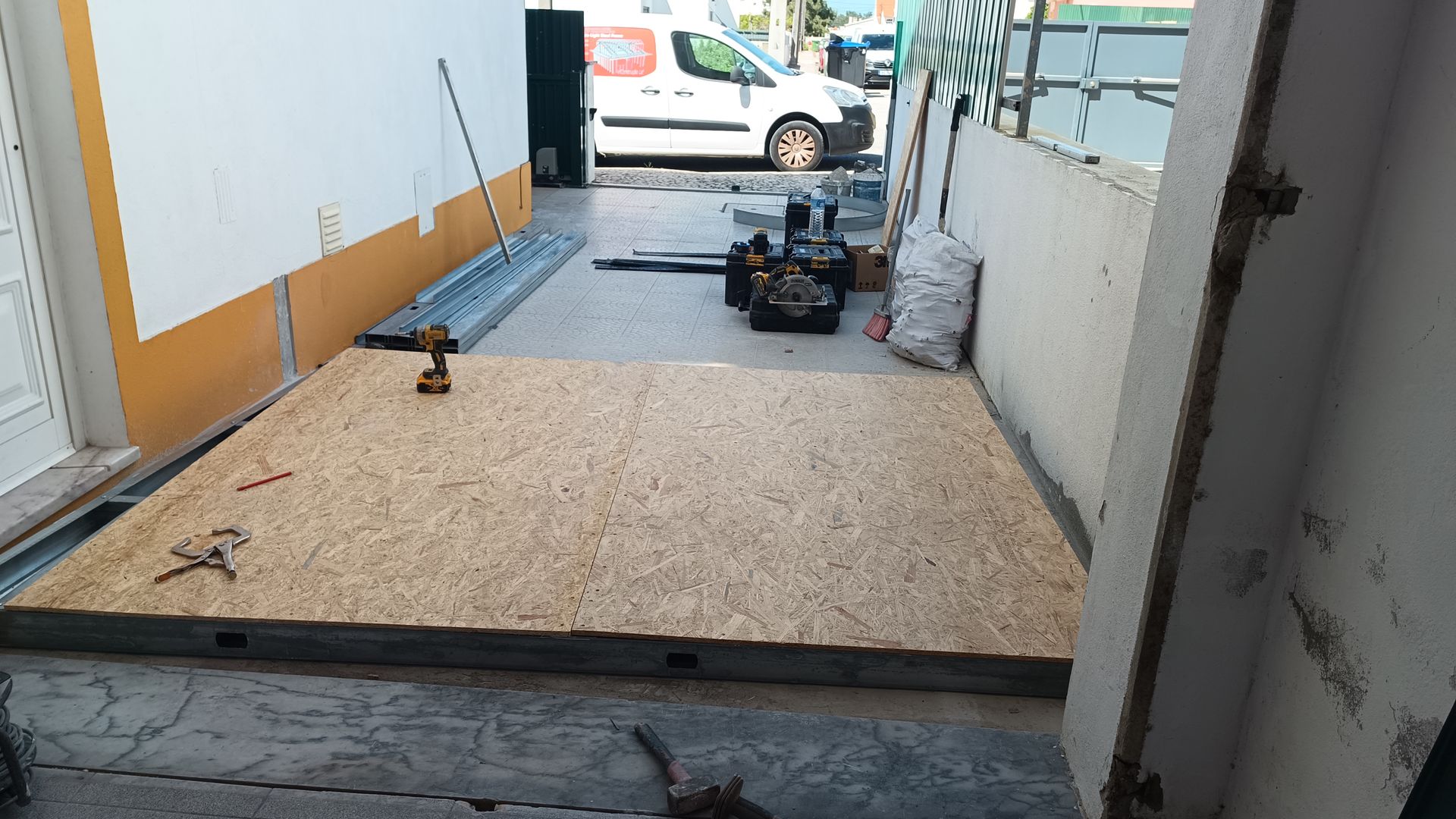Placa OSB sobre uma superfície de concreto, ferramentas e uma van em uma área de construção.