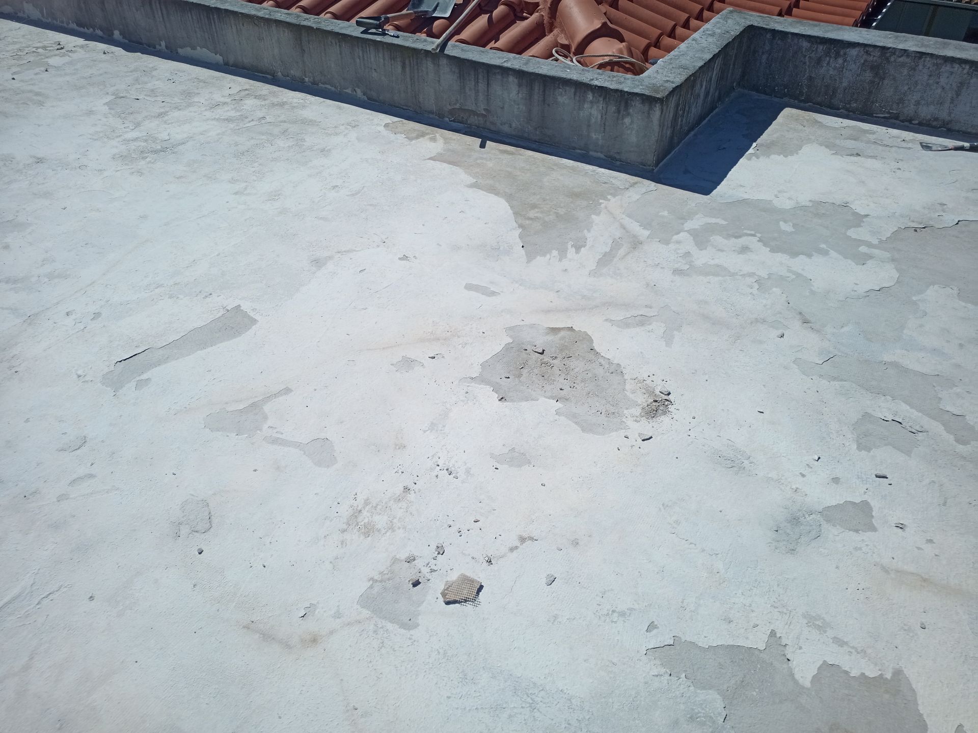 Telhado plano de concreto com áreas descascadas, adjacente a uma parede e telhado de telhas.