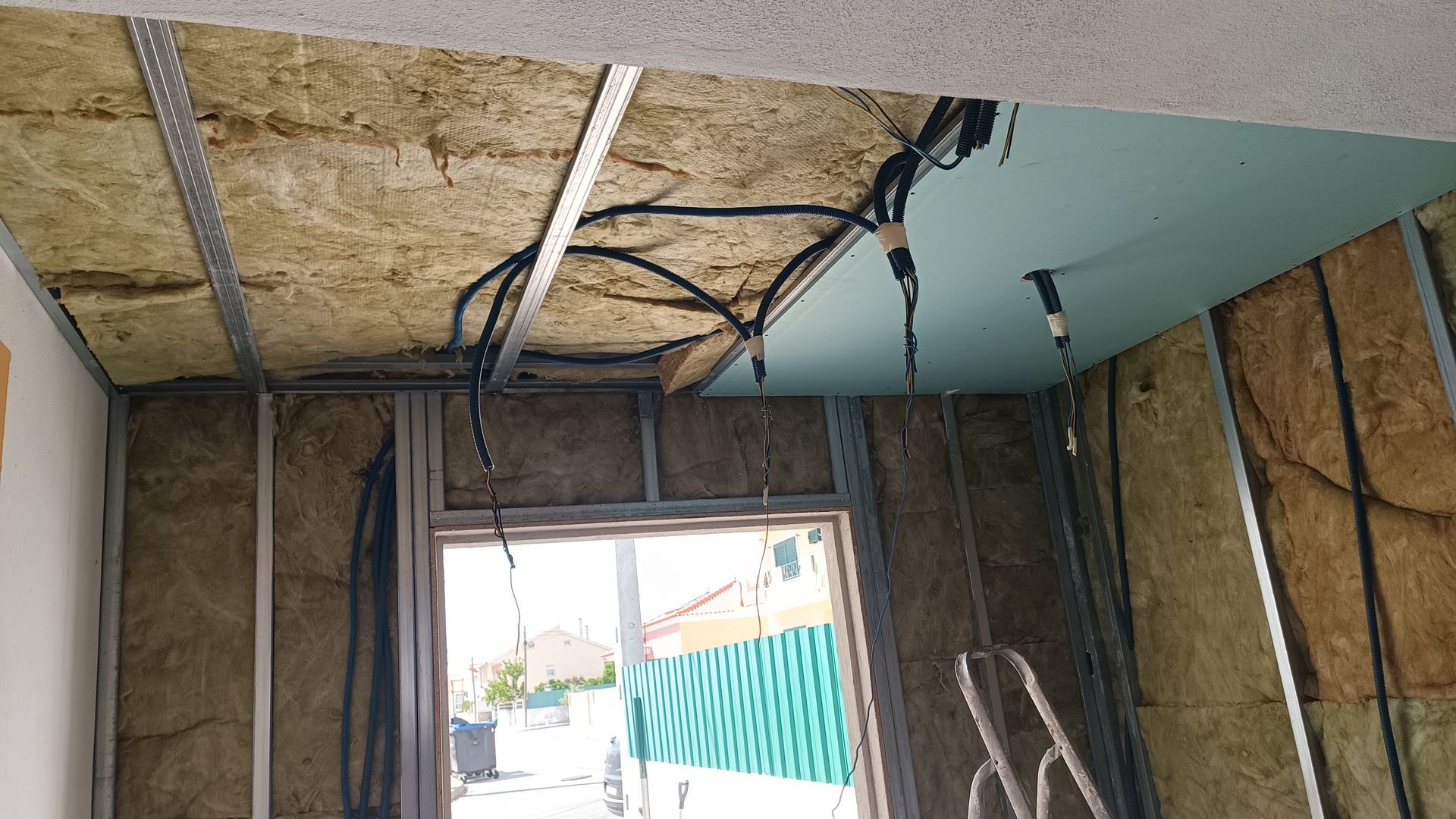 Construção interna com isolamento, fiação e drywall expostos ao redor de uma janela.