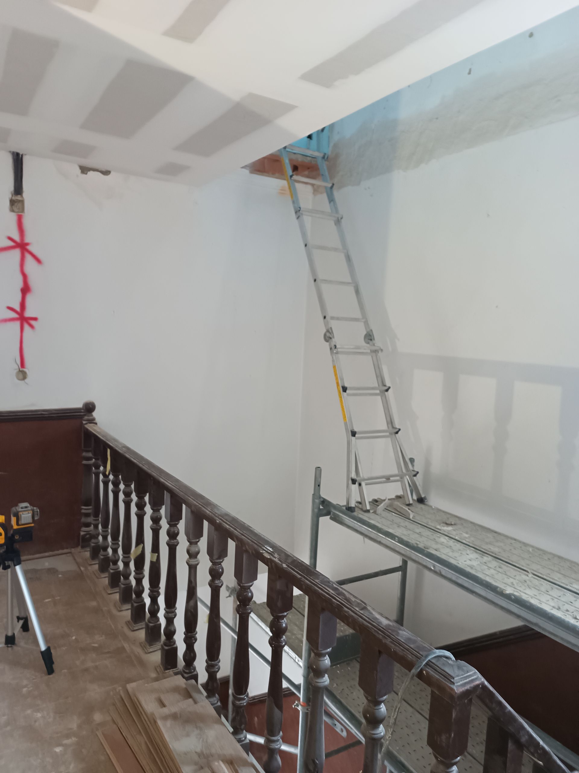 Escada em andaime que dá acesso a uma abertura no teto de uma sala em construção.