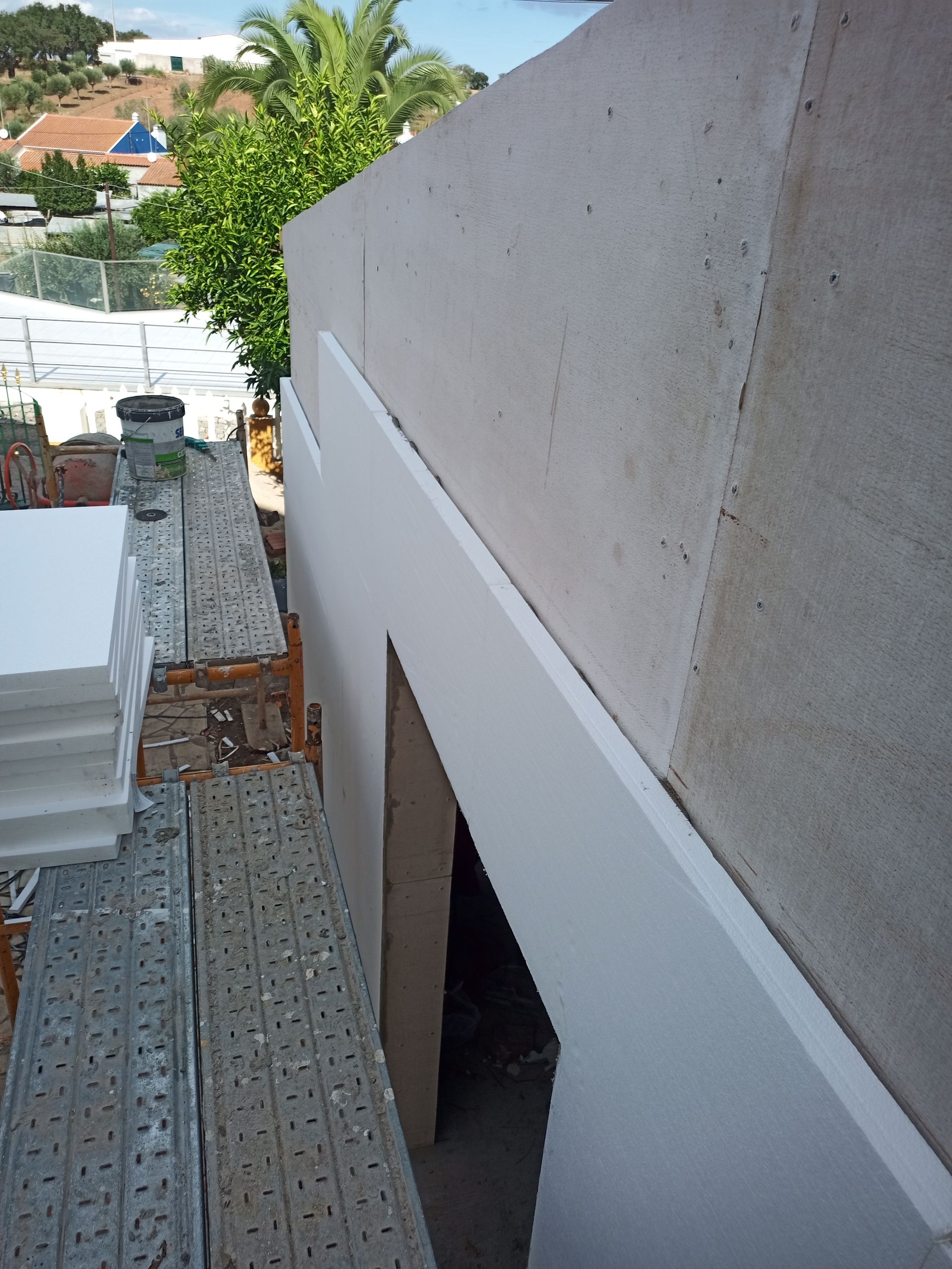 Canteiro de obras: instalação de isolamento de espuma branca na parte externa do edifício, com andaimes à vista.