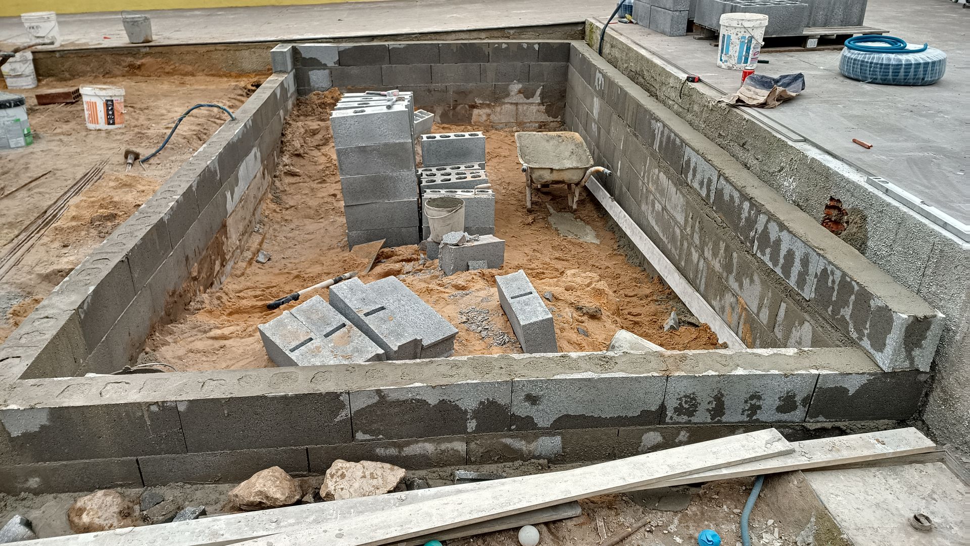 Canteiro de obras com paredes de fundação em blocos de concreto e base de areia.