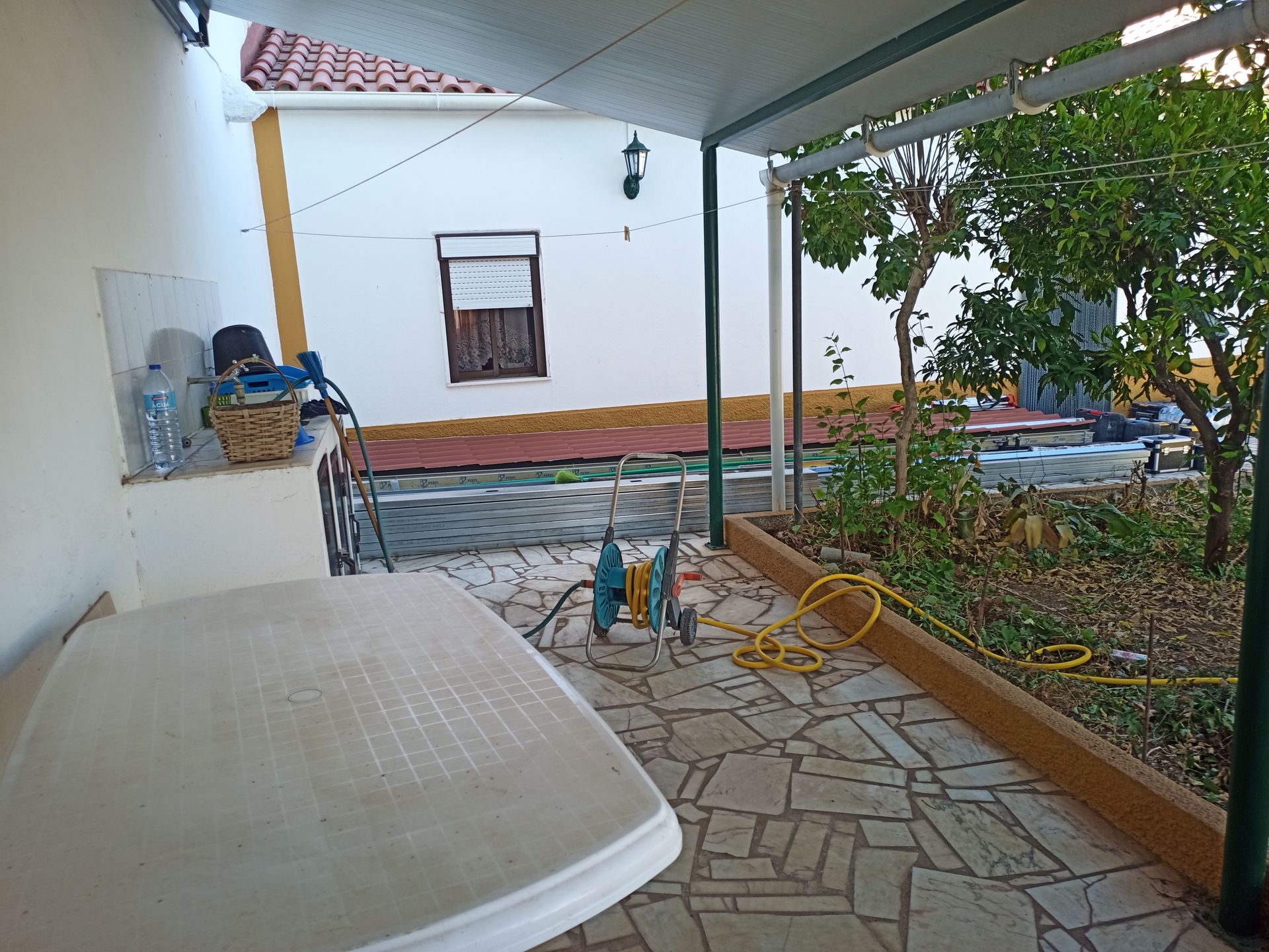 Pátio com mesa, ferramentas, jardim e prédio branco ao fundo.