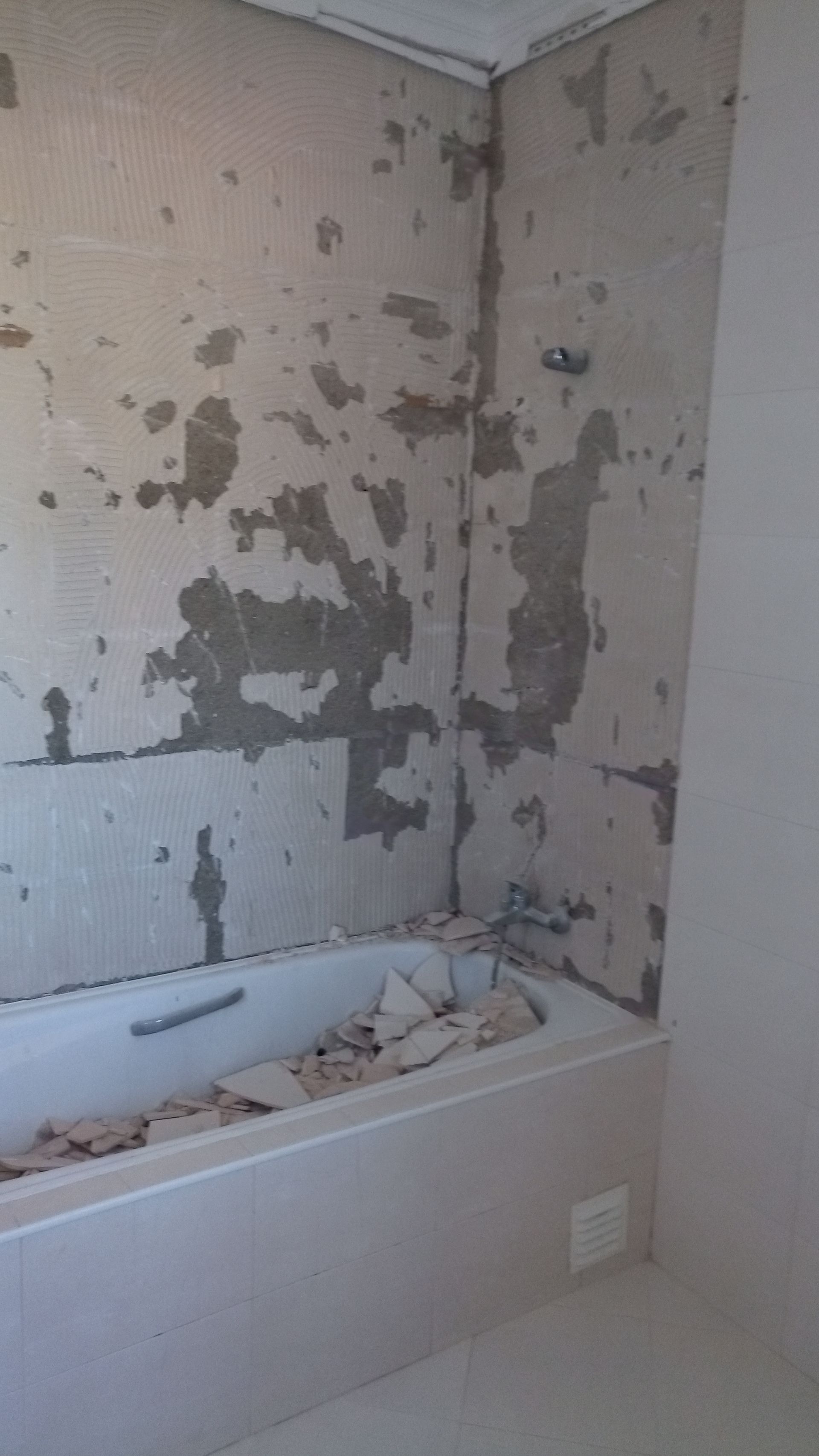 Banheiro com banheira, paredes com azulejos e gesso descascados, reforma inacabada.