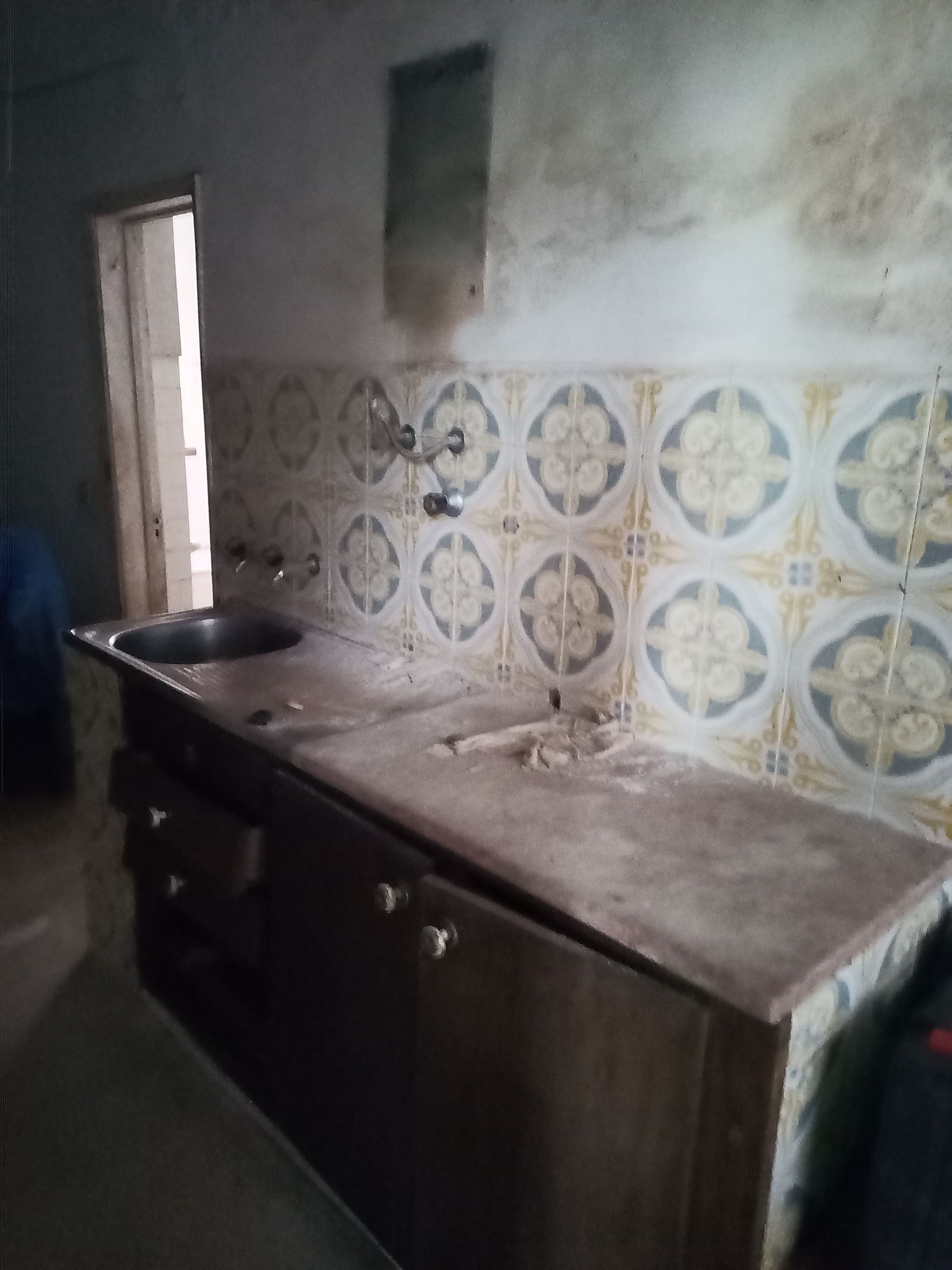 Cozinha com azulejos na parede, pia e armários. As paredes são de cor clara.
