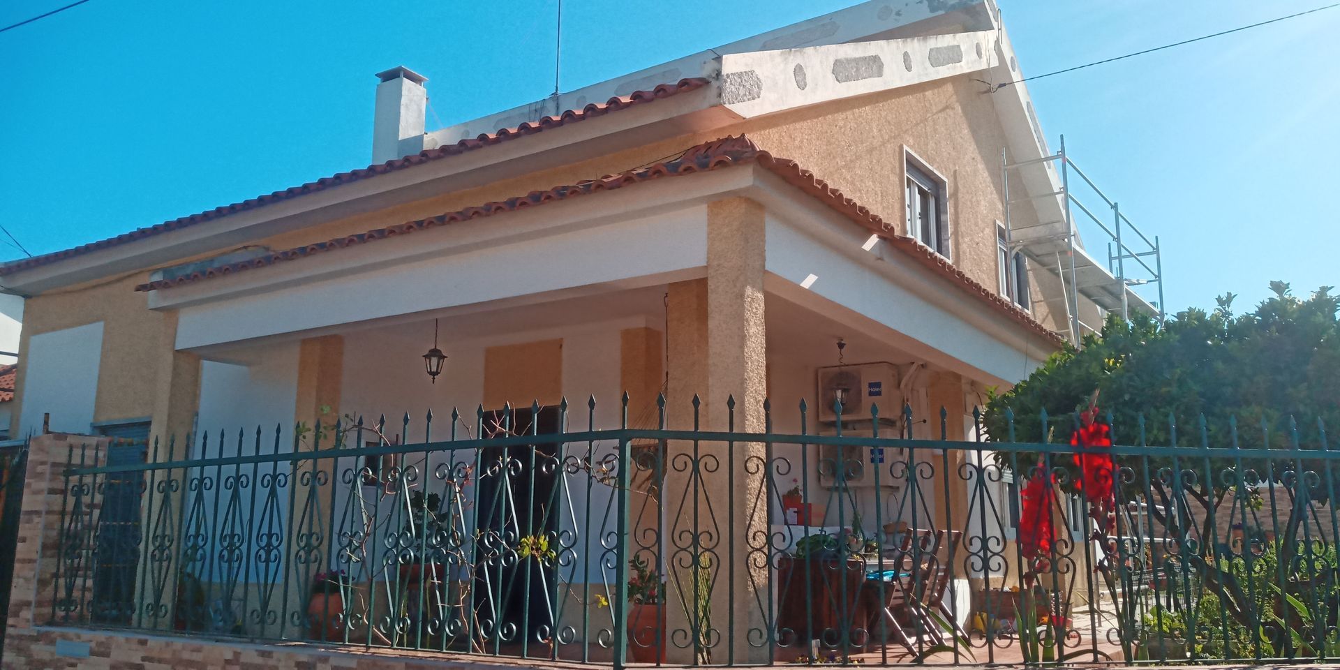Casa amarela com cerca de ferro, telhado vermelho e céu azul.