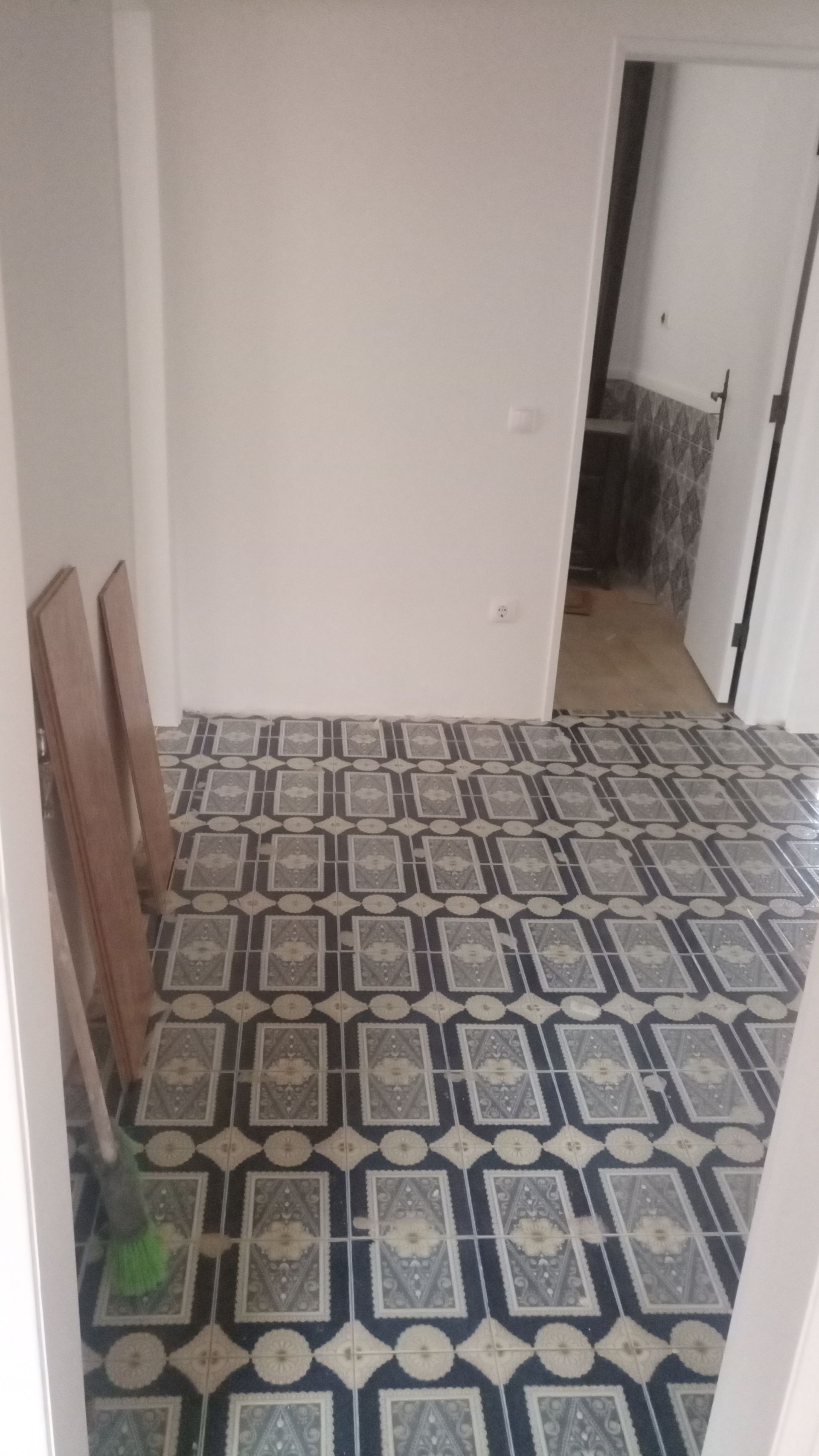 Interior de quarto com piso de ladrilho estampado, paredes brancas e porta.