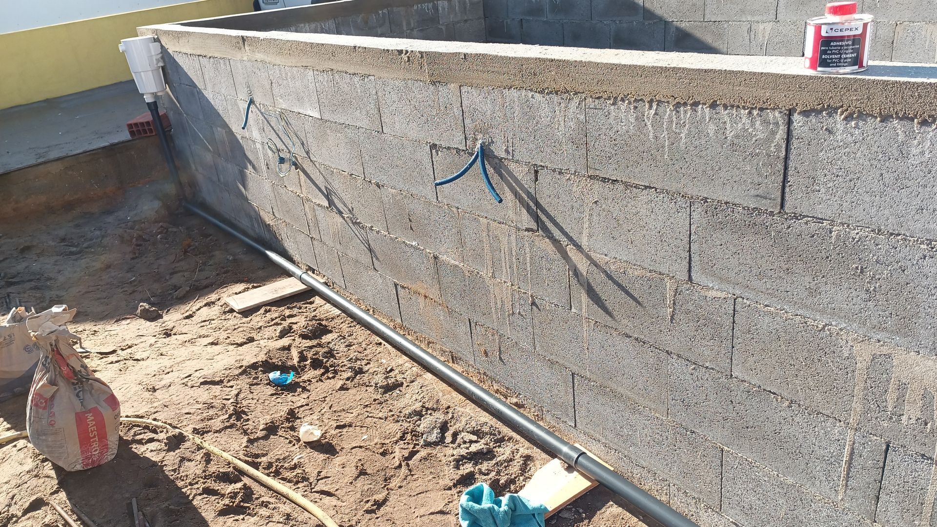 Uma parede de blocos de concreto em construção com conduítes elétricos expostos e fiação azul.